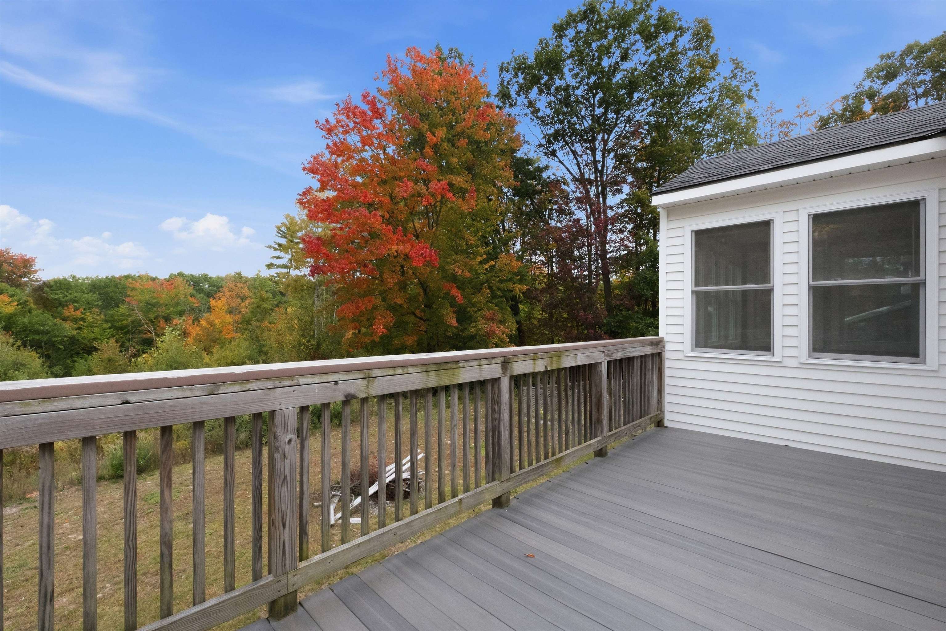 Deck with gray flooring and wooden railing overlooking colorful autumn trees.