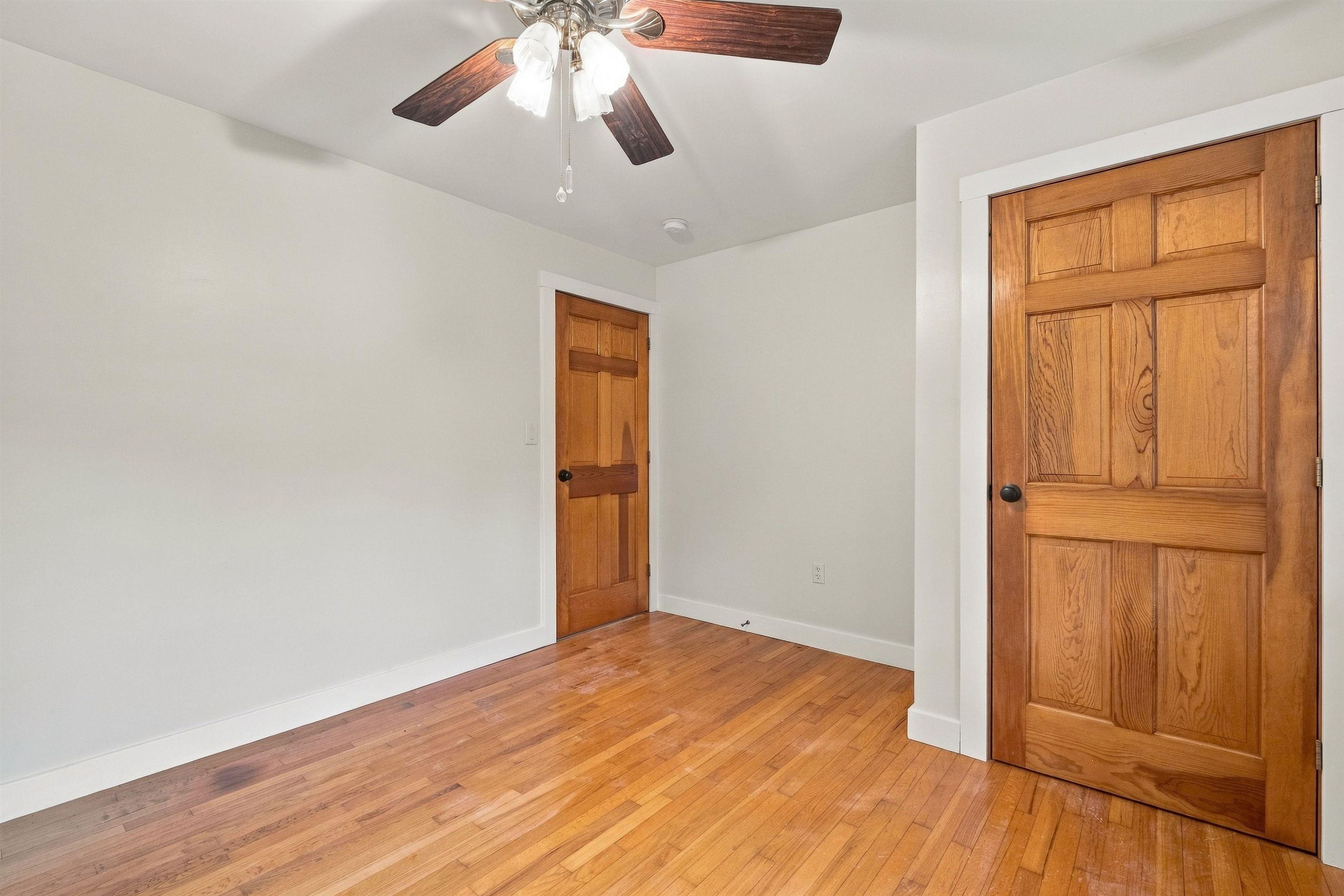 Vacant room with hardwood floors, two wooden doors, and a ceiling fan.