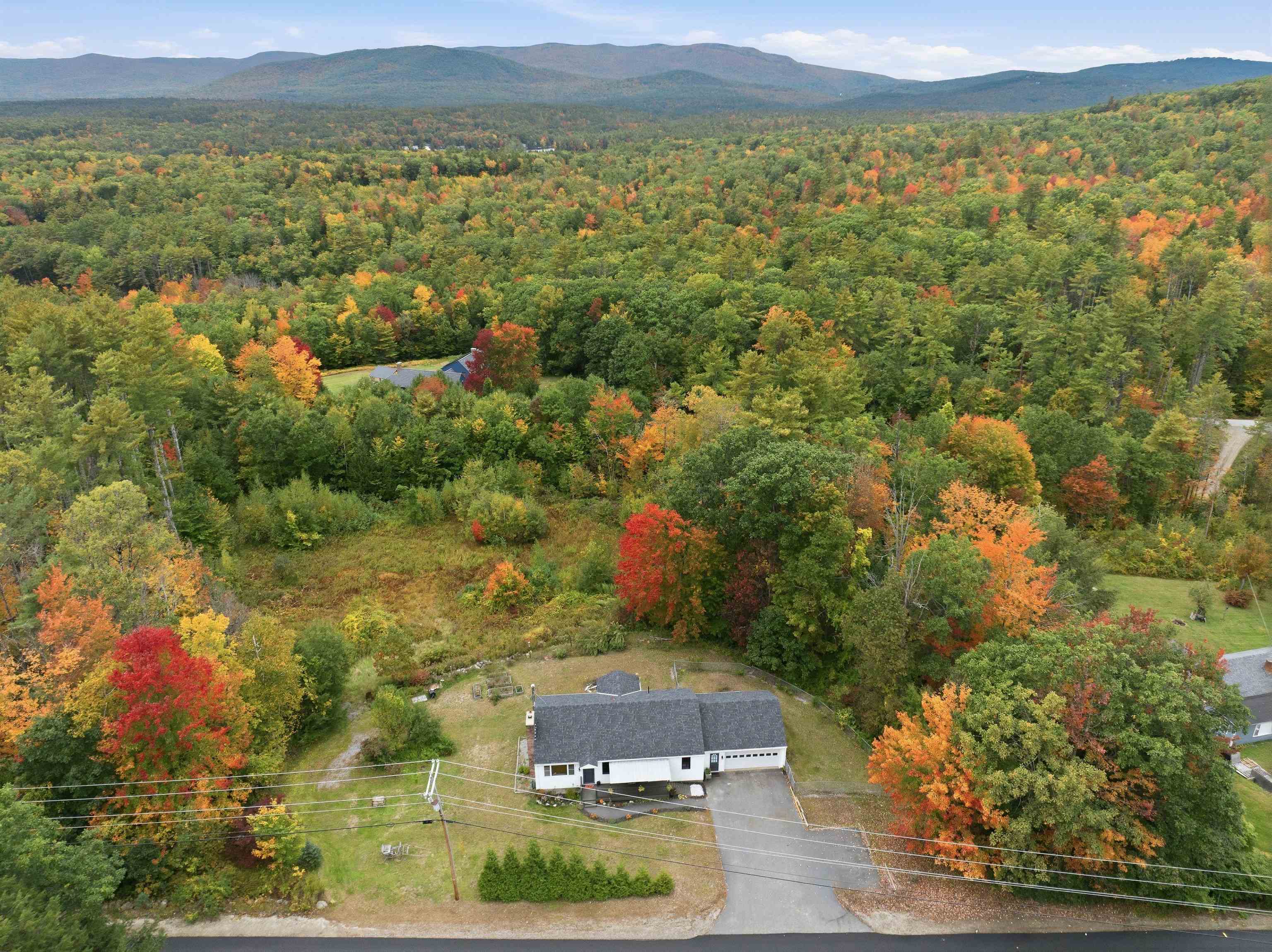 Aerial view of a white home amid autumn woods, with mountains on the horizon.