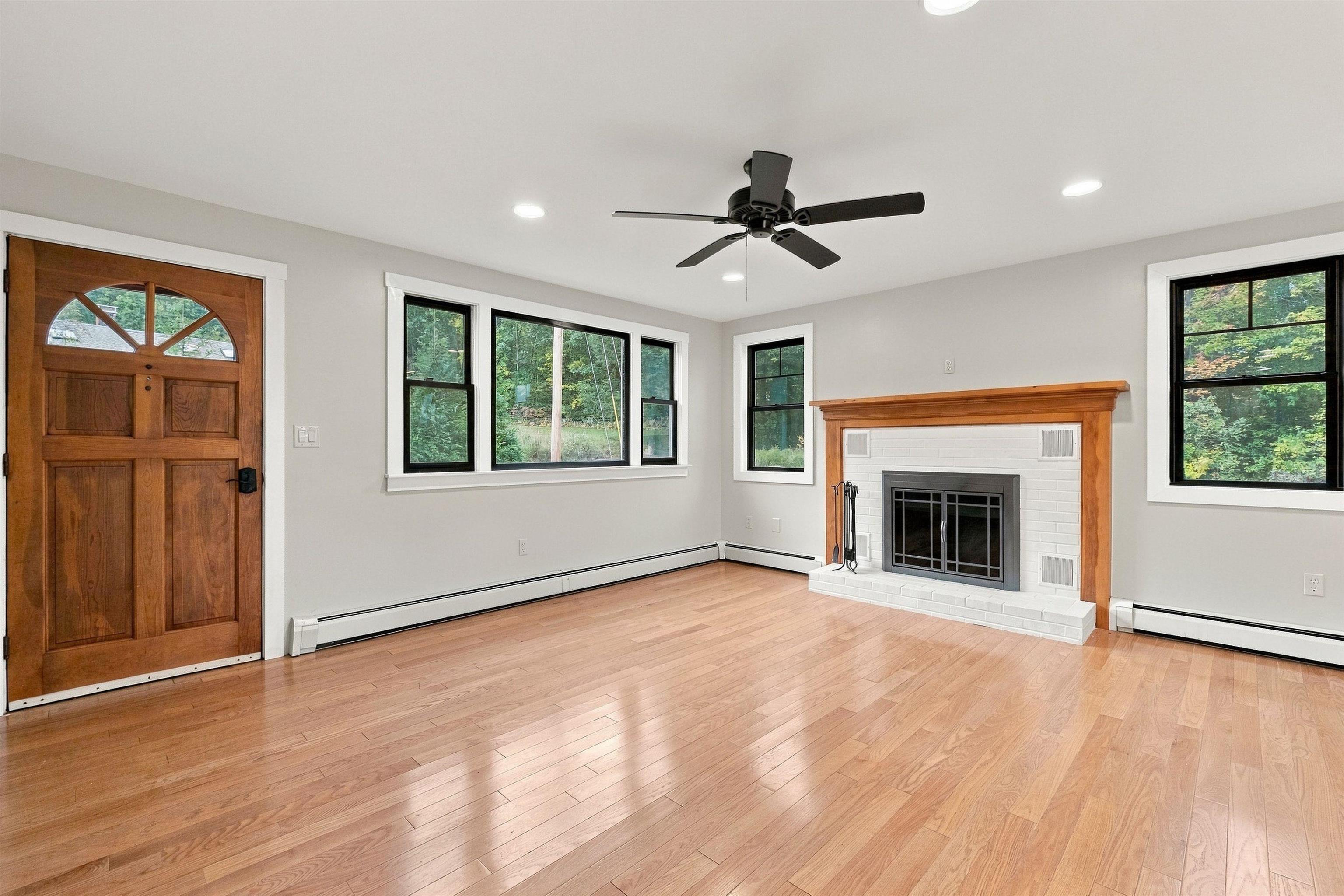 Empty living room with hardwood floors, a white brick fireplace, and an arched wooden entry door.