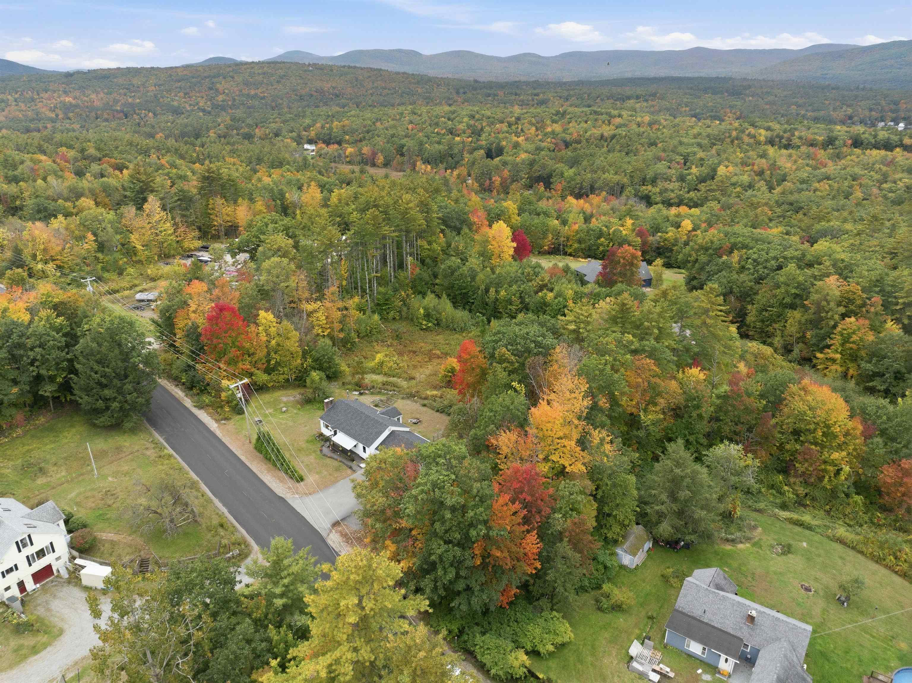 Aerial view of homes amid autumn woodland, with mountain ridges in the distance.
