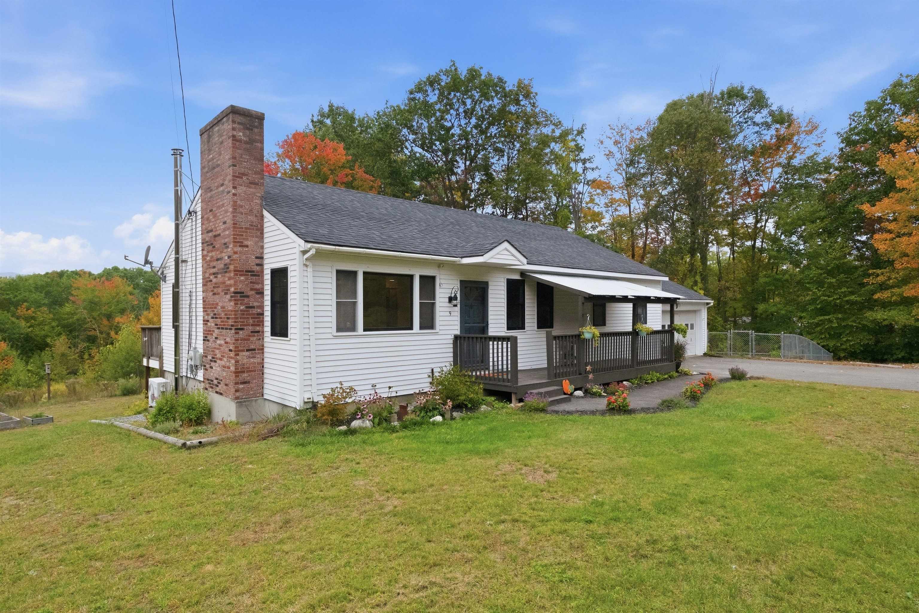 White single-story house with a tall brick chimney, covered porch, and autumn trees behind it.