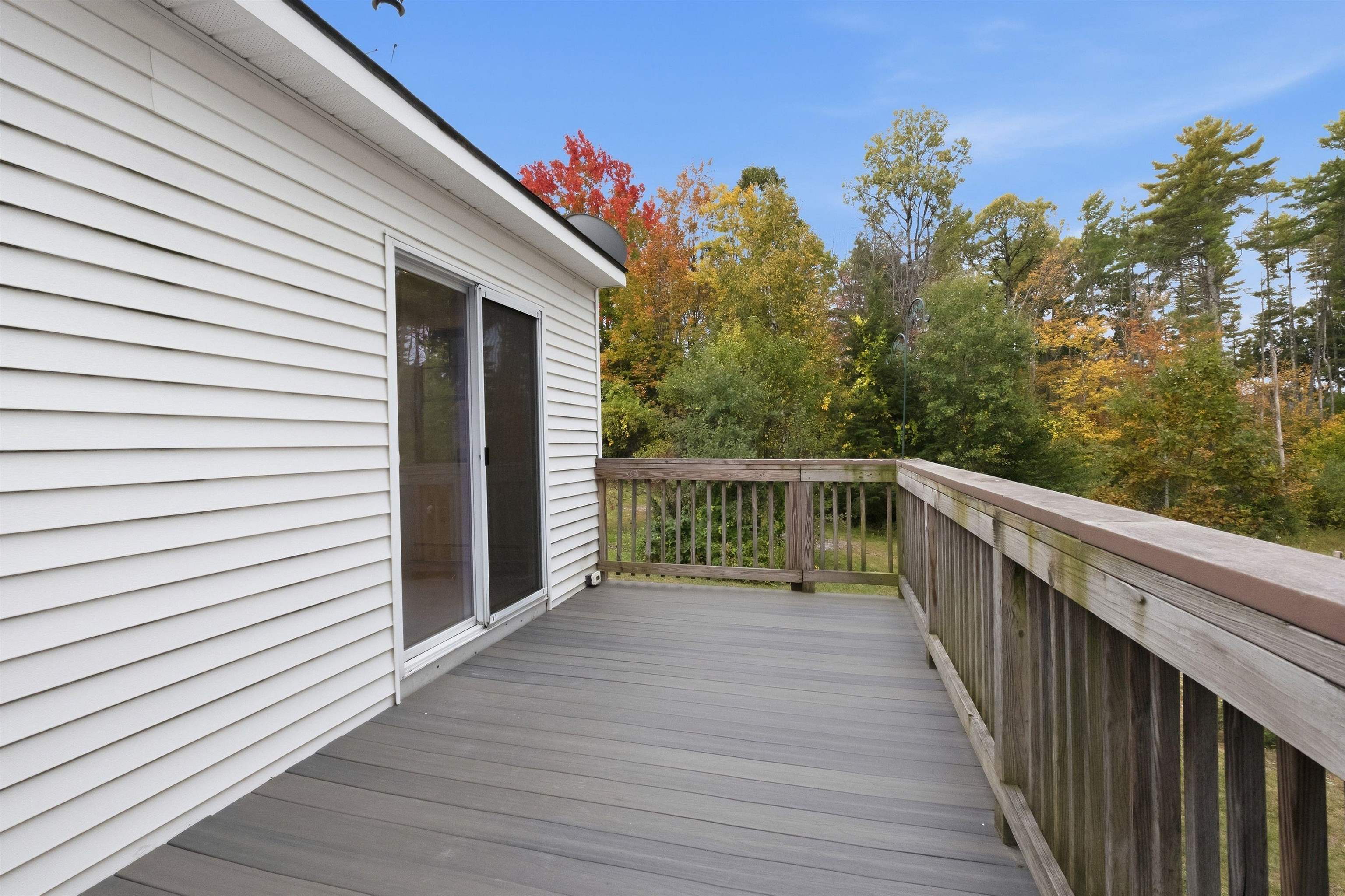 Deck with gray flooring, wooden railing, and views of autumn trees.