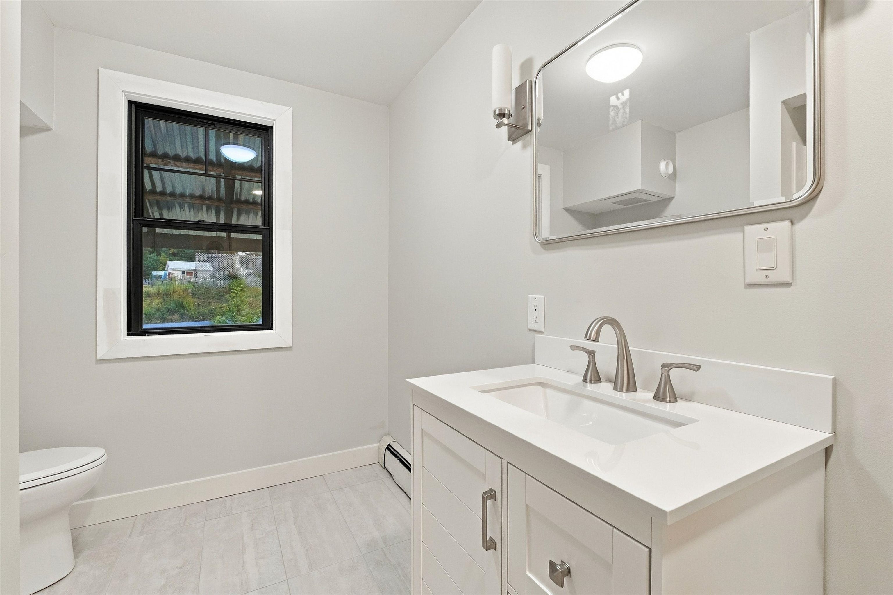 Bathroom with a white vanity, large mirror, tiled floor, and black-framed window.