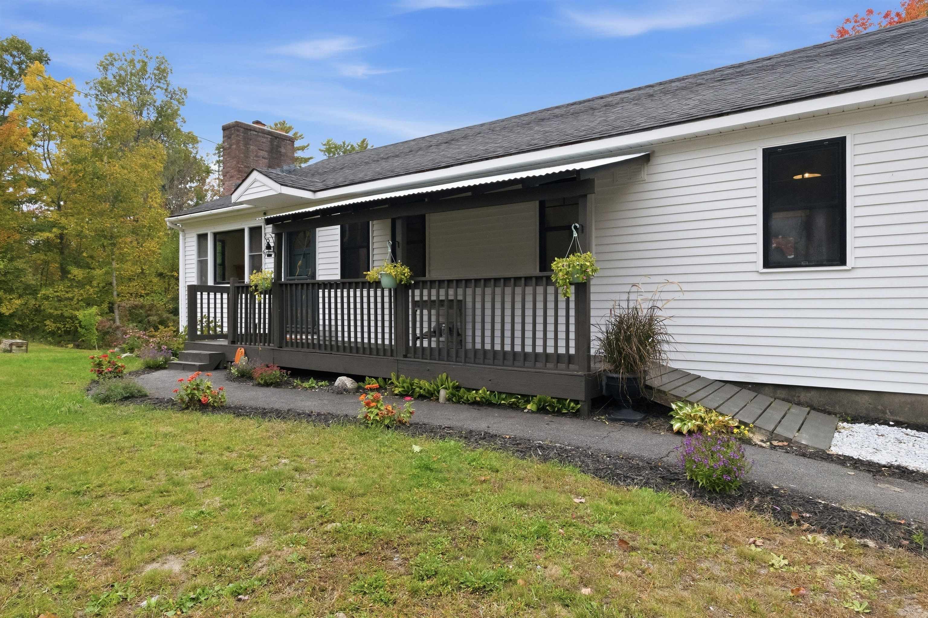White-sided house with a long covered porch, dark railing, and flower beds along the lawn.