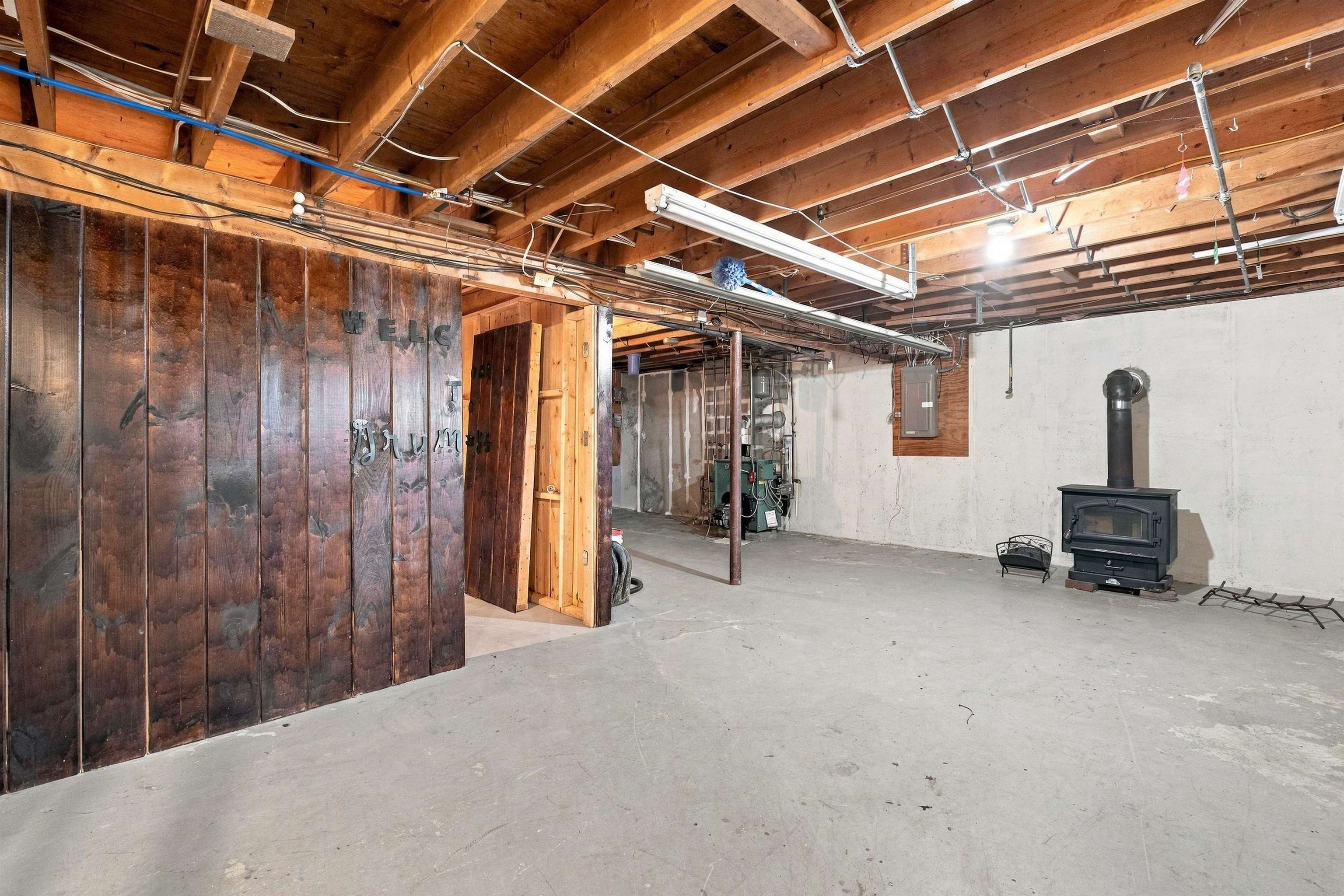 Unfinished basement with exposed ceiling joists, utility equipment, and a freestanding wood stove.