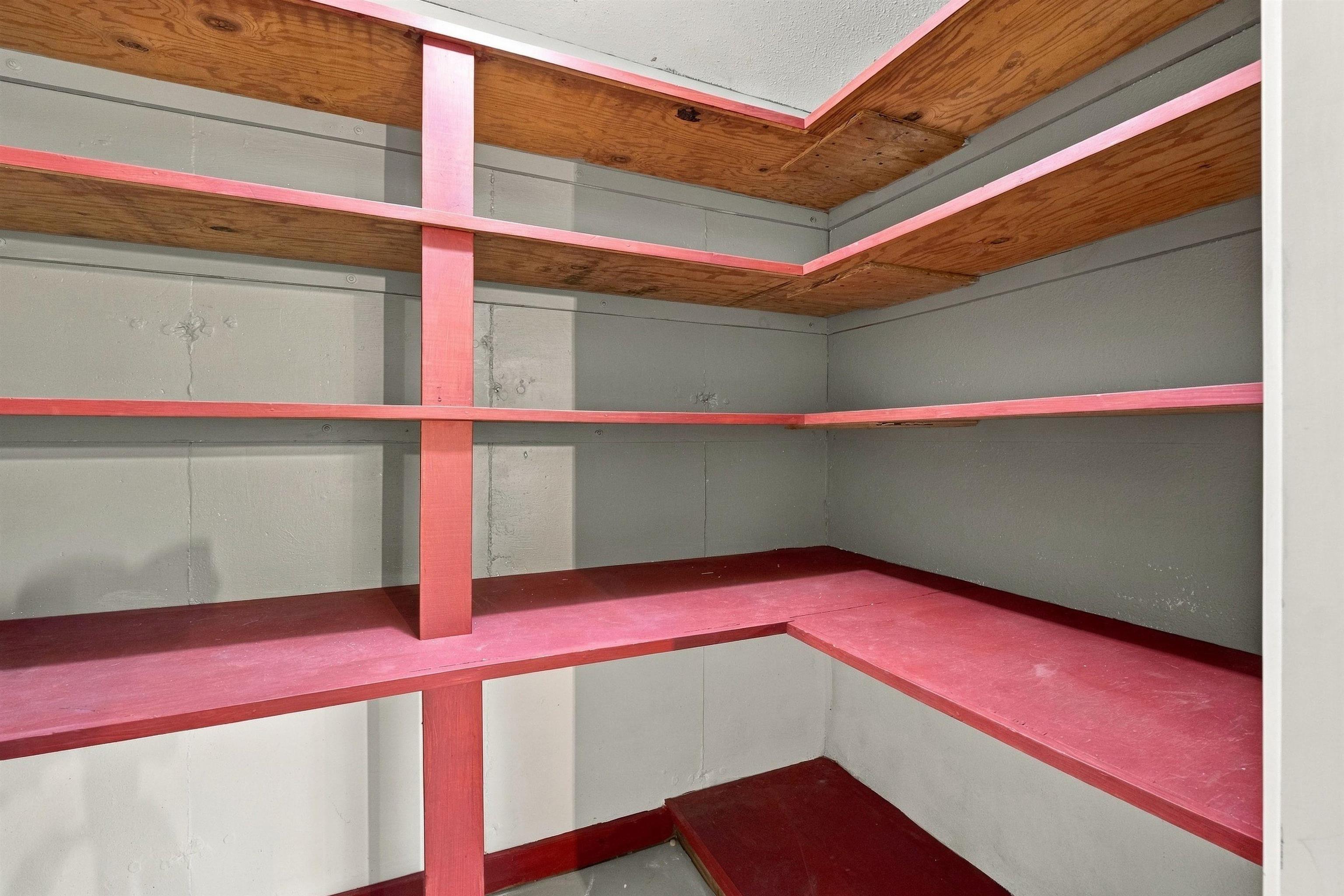 Empty red-painted wooden shelves wrap around the gray walls of a storage area.