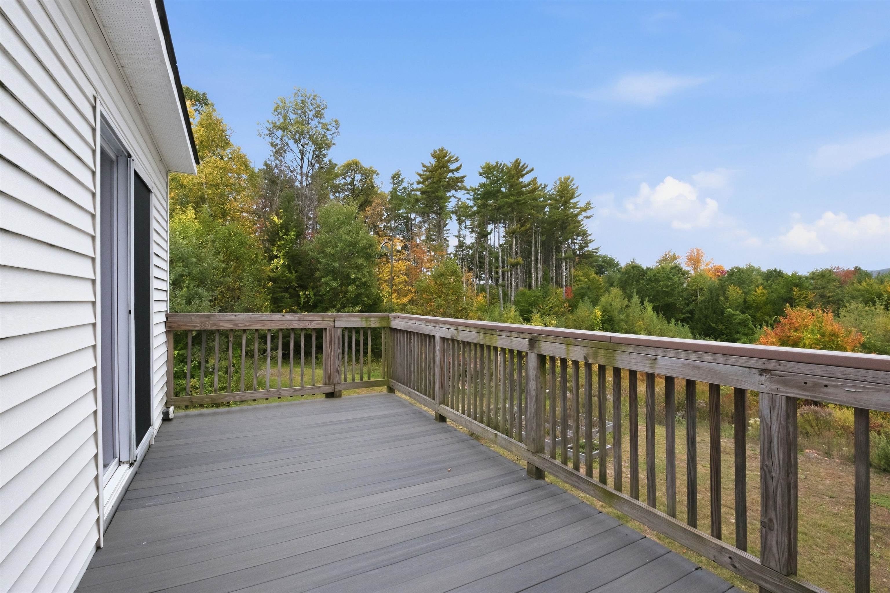 Gray deck overlooking autumn trees and woods, with white siding and wooden railings.