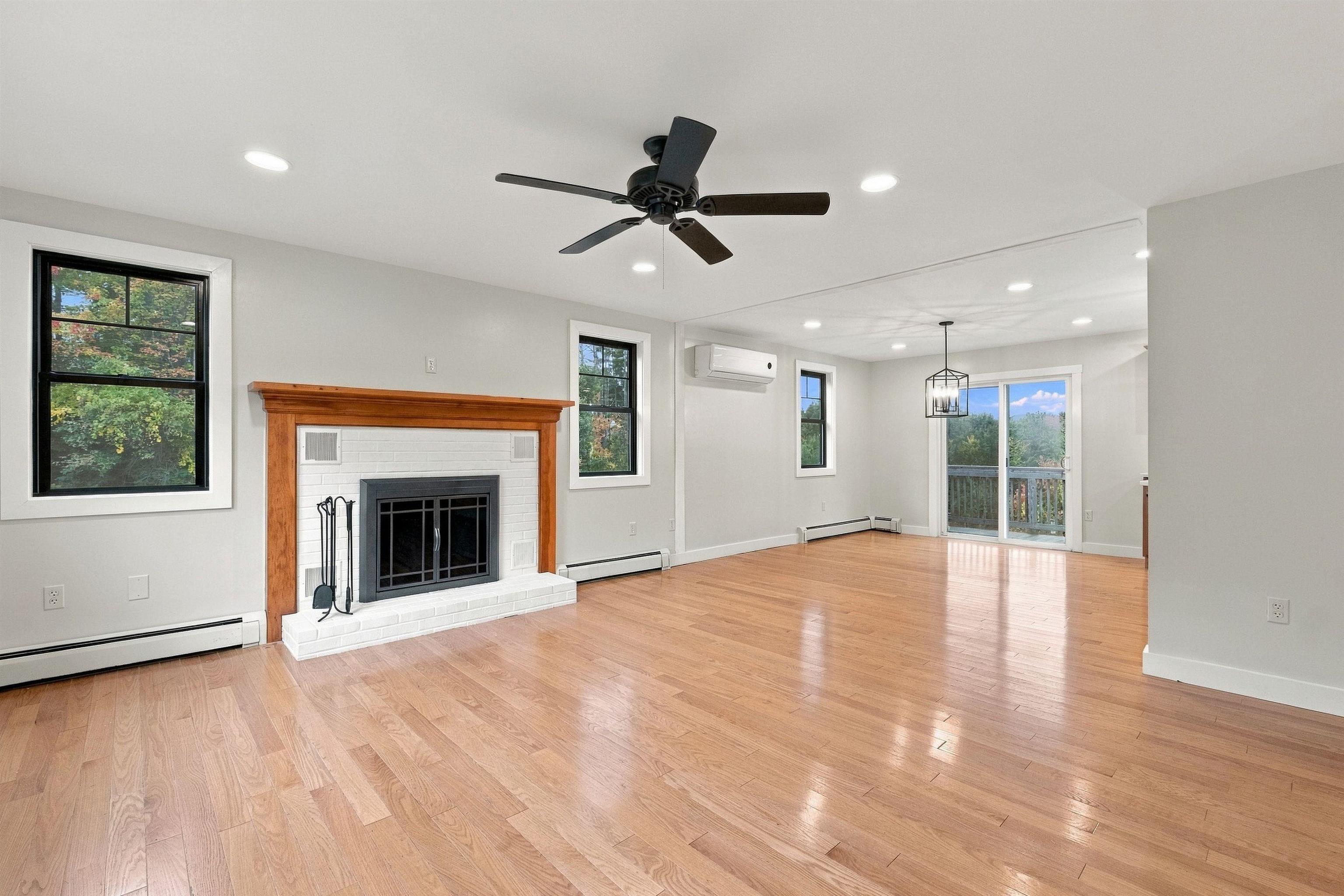 Vacant living room with hardwood floors, a wood-framed fireplace, and sliding glass doors to a deck.