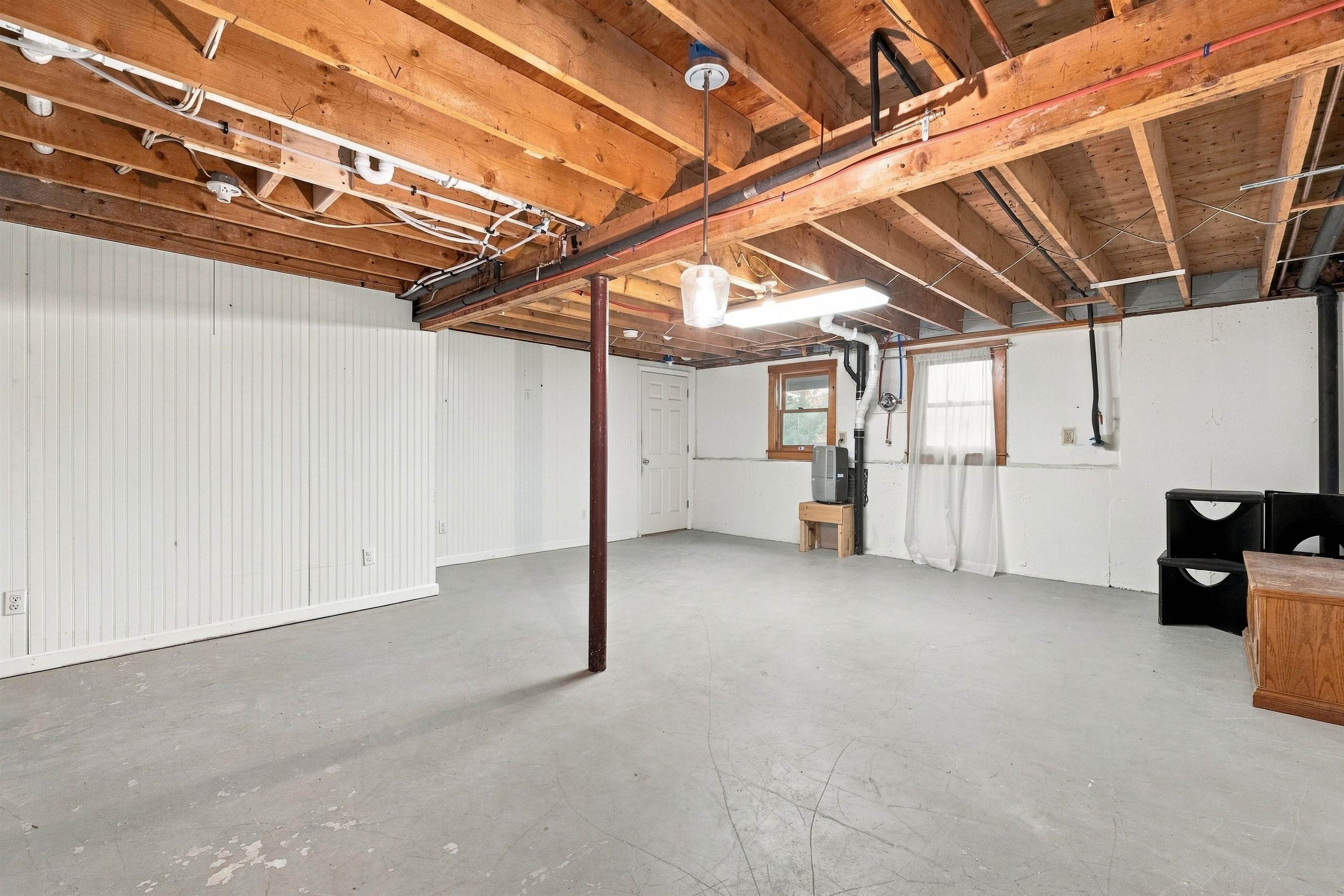 Open basement with a concrete floor, exposed wooden ceiling joists, and a central support post.