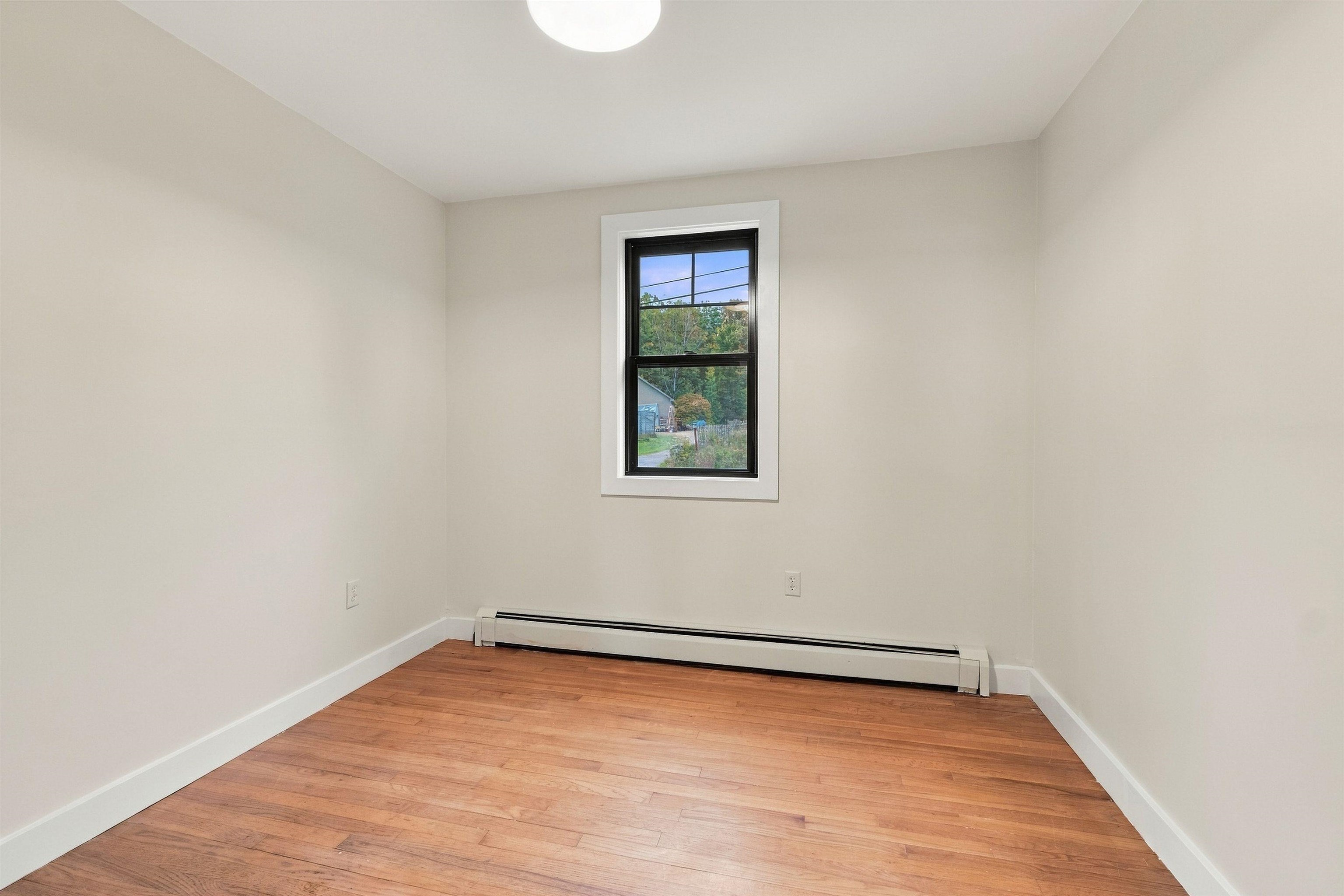 Vacant room with hardwood floors, a black-trimmed window, and a baseboard heater.