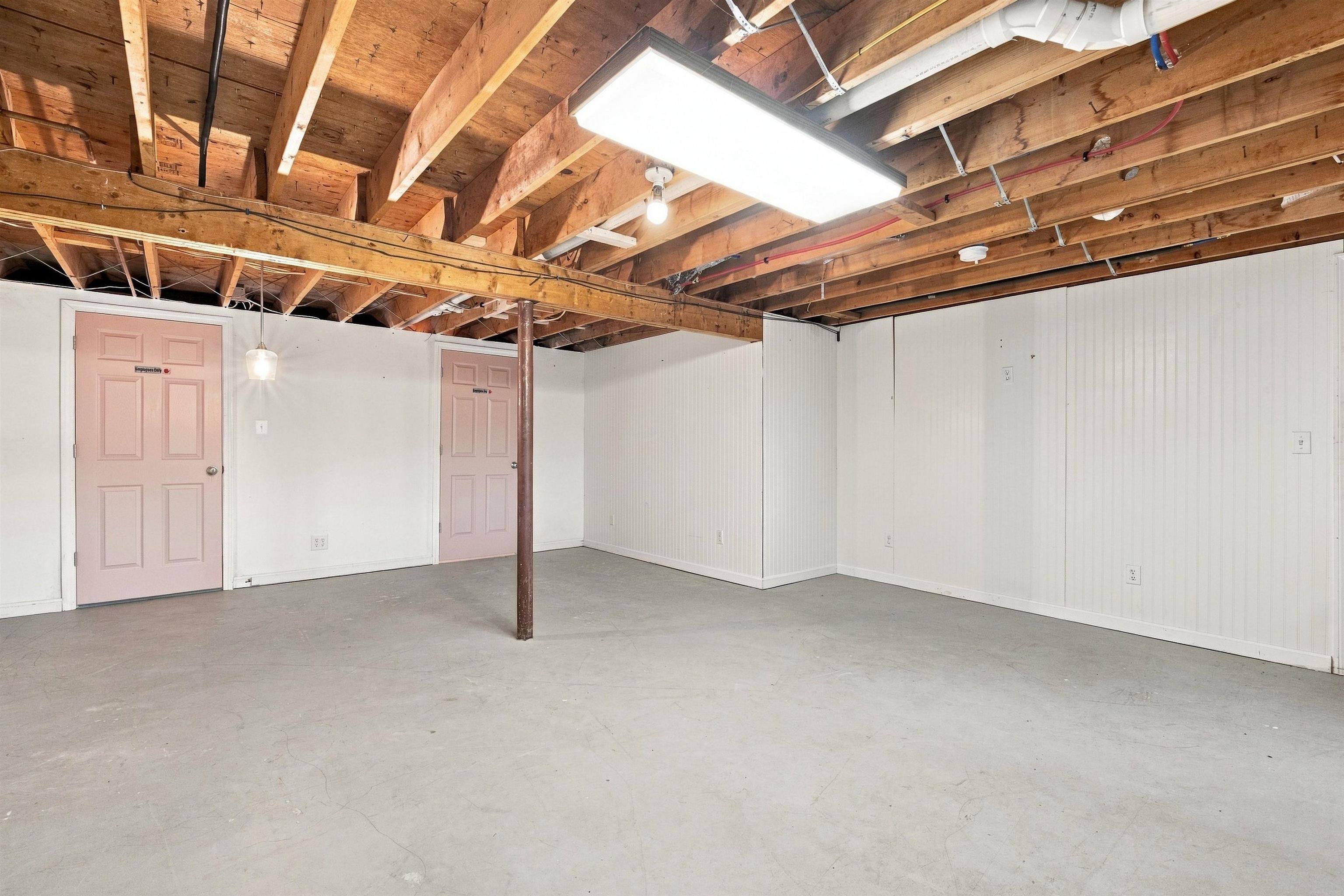 Empty basement with exposed wooden ceiling joists, a concrete floor, and two pink doors.