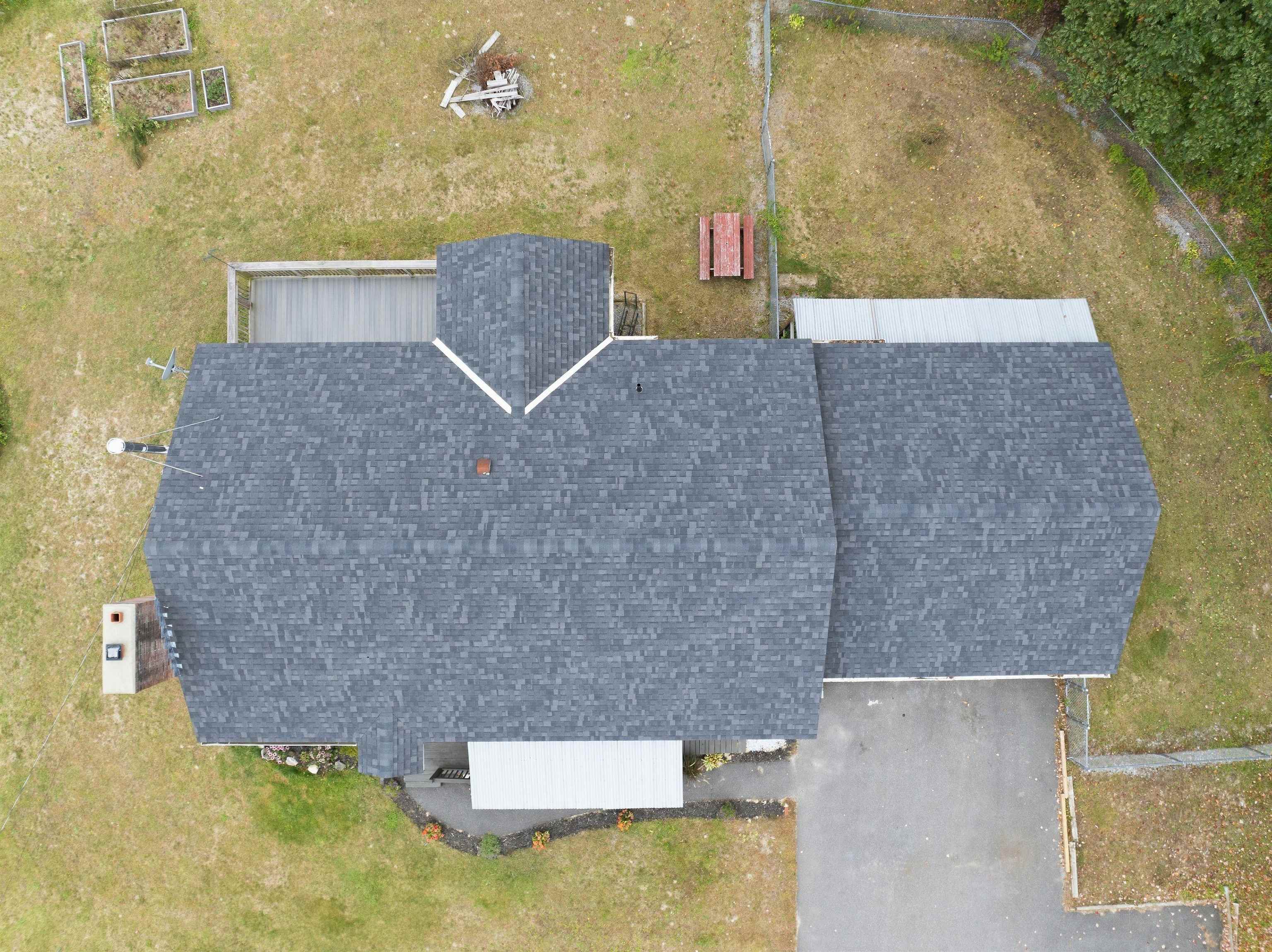 Aerial view of a house with a broad gray shingle roof, lawn, and paved driveway.