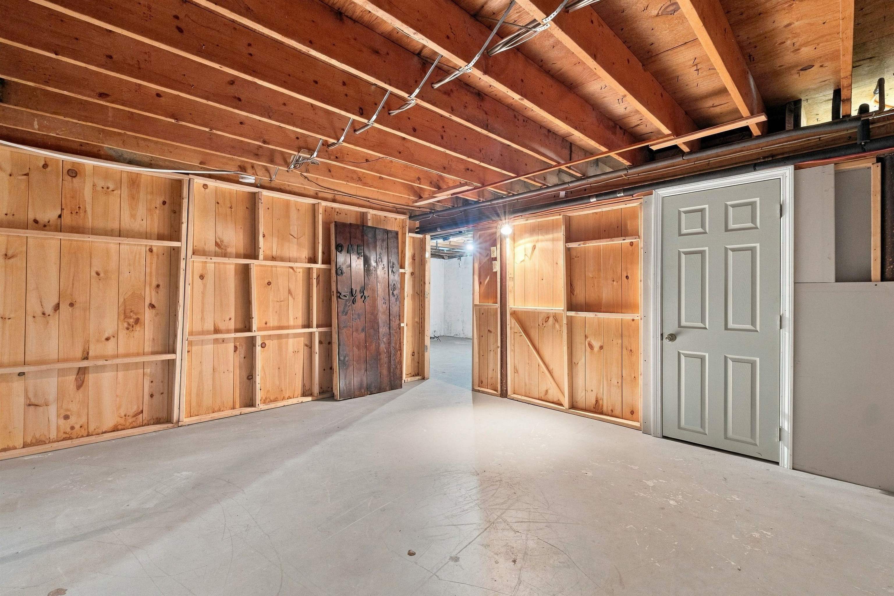 Unfinished basement with exposed joists, wooden shelving, and a concrete floor.