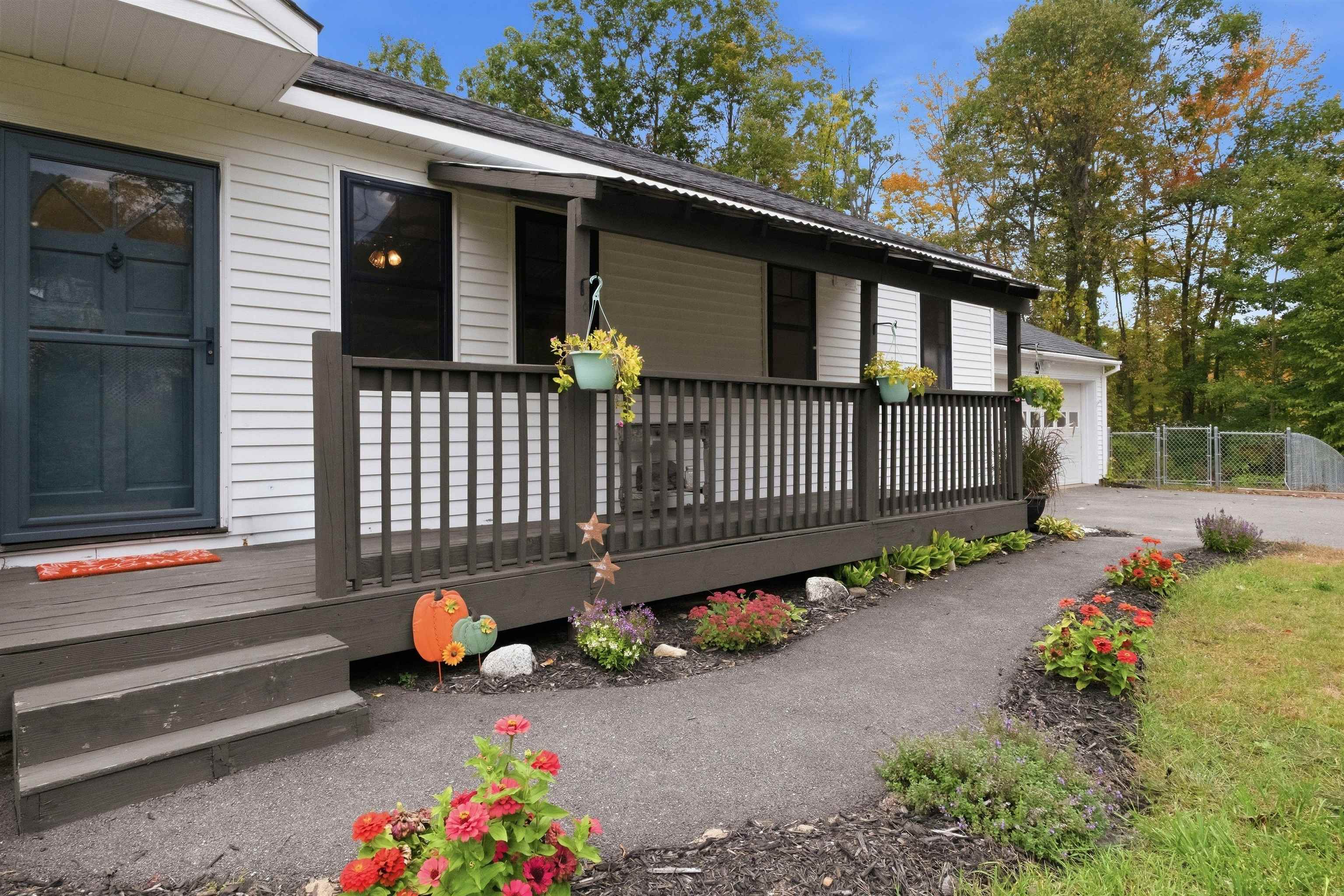 White-sided home with a long dark-railed porch, hanging flower baskets, and colorful garden beds.