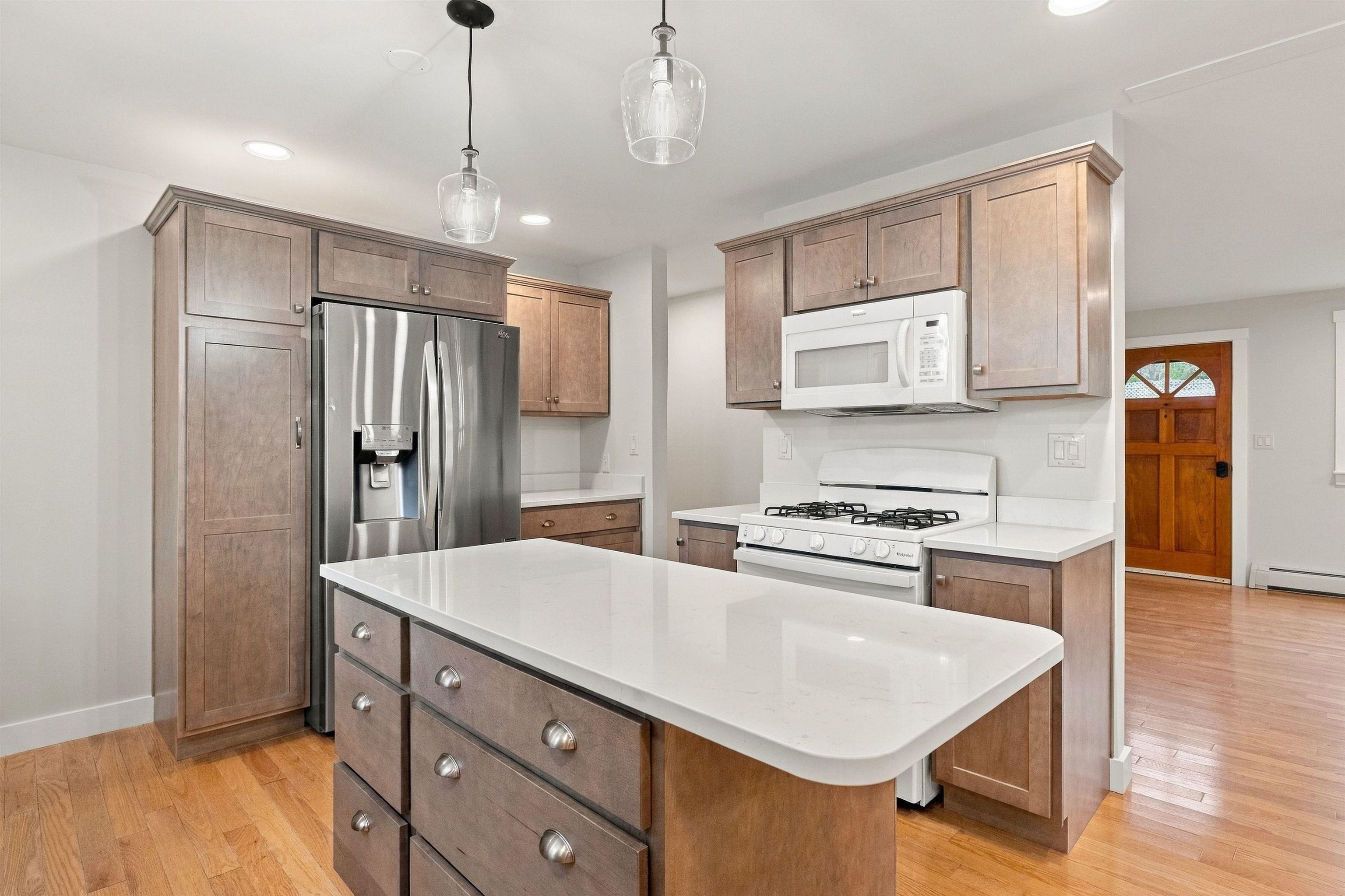 Kitchen with a large quartz island, warm wood cabinets, stainless refrigerator, and gas range.