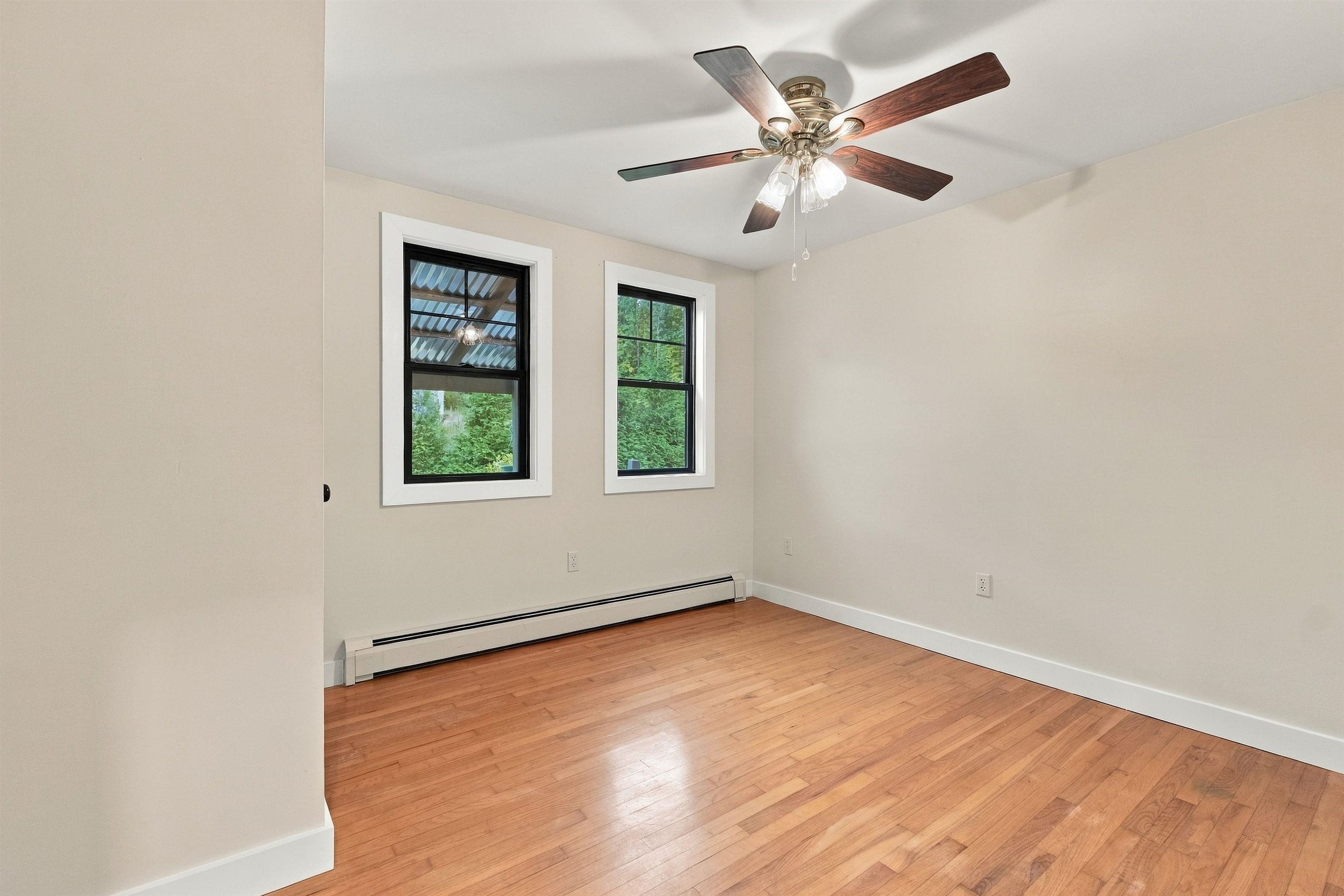 Empty room with hardwood floors, two windows, and a ceiling fan with lights.