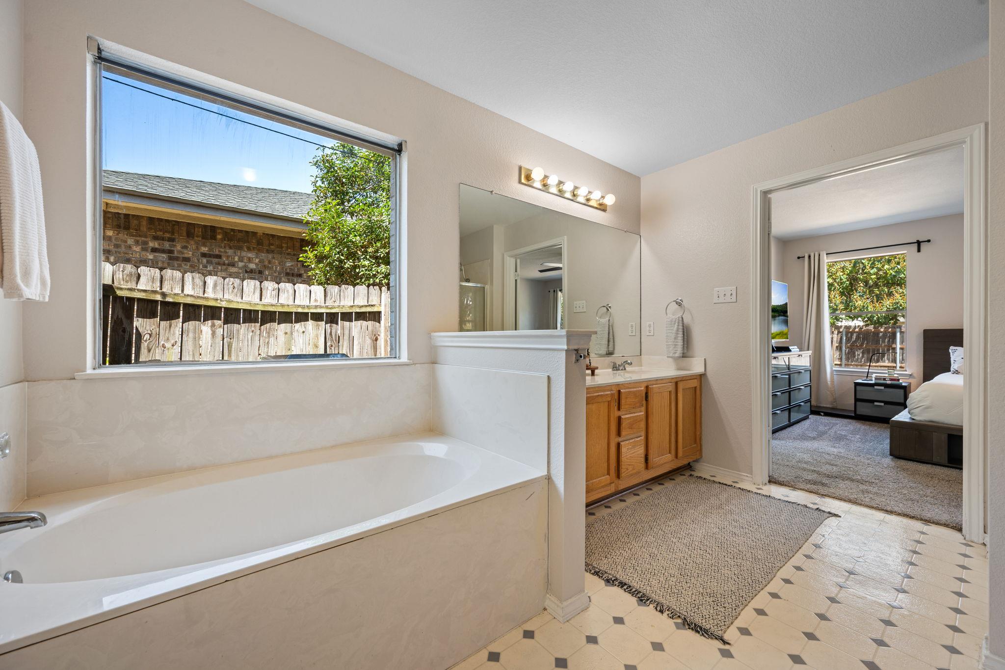 Bathroom with a large window-side tub, wood vanity, and doorway into a bedroom.