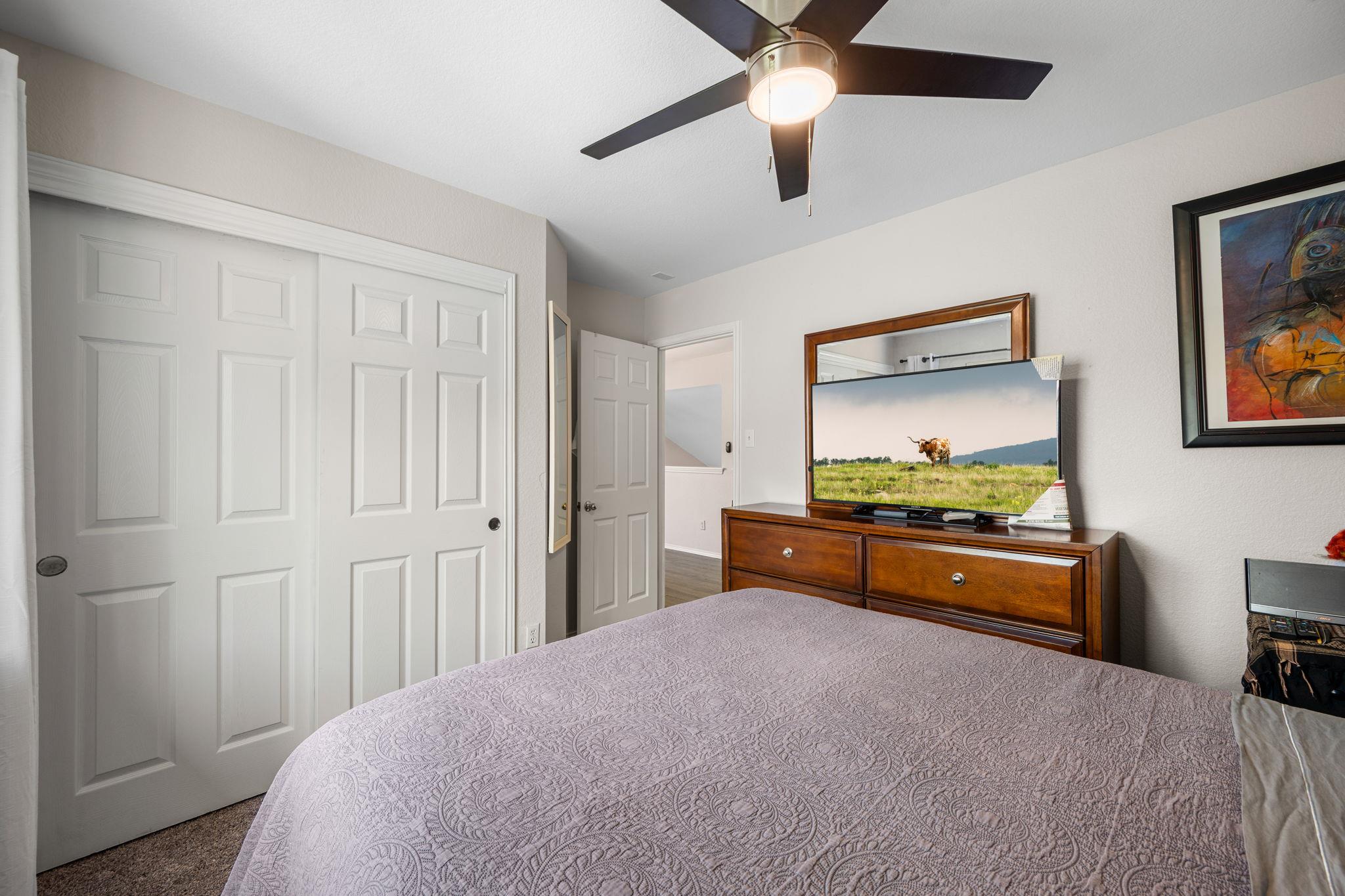 Bedroom with a patterned quilt, paneled closet doors, and a television on a wooden dresser.