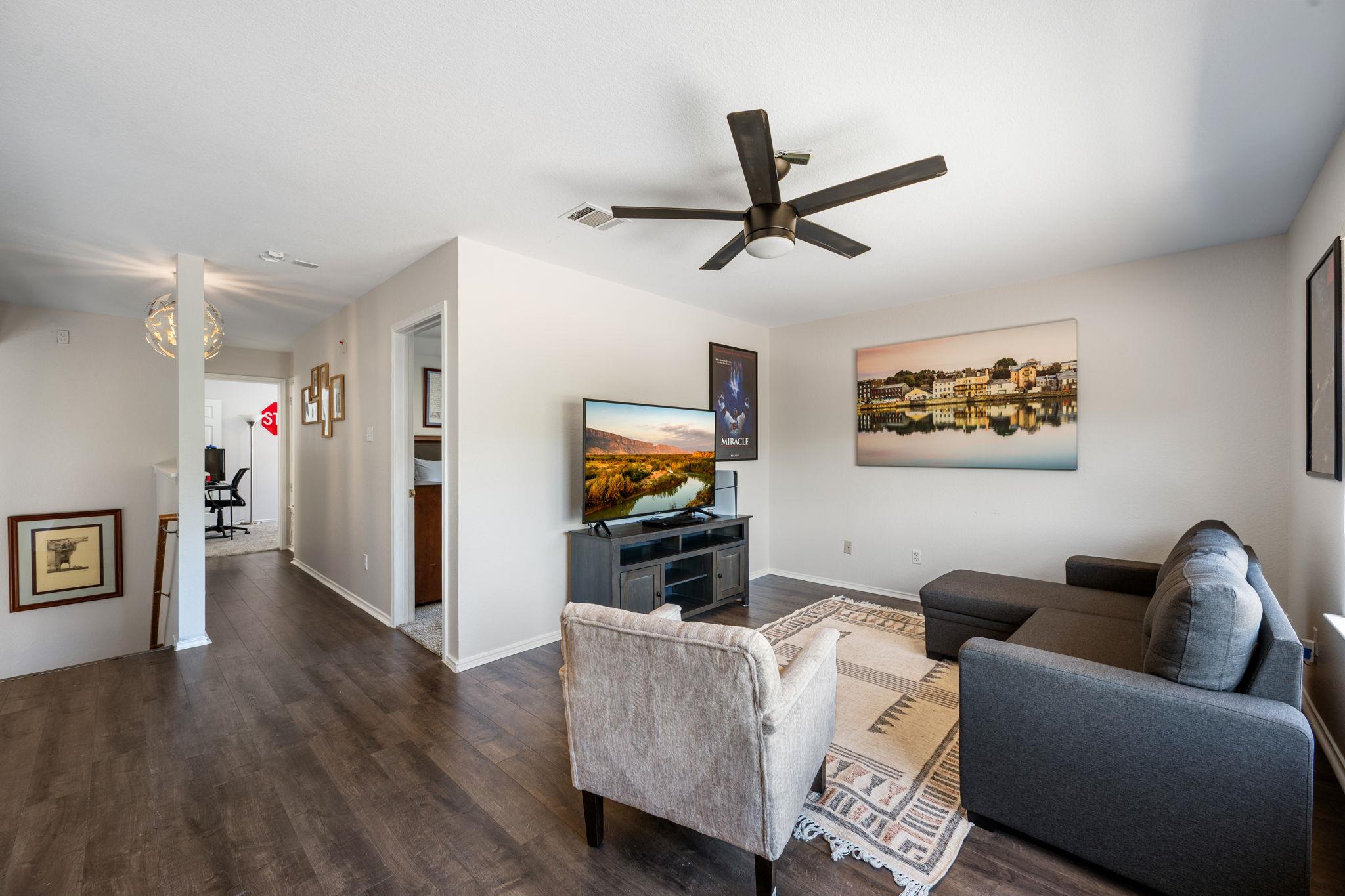 Furnished living room with gray sectional, patterned rug, and television beneath a ceiling fan.