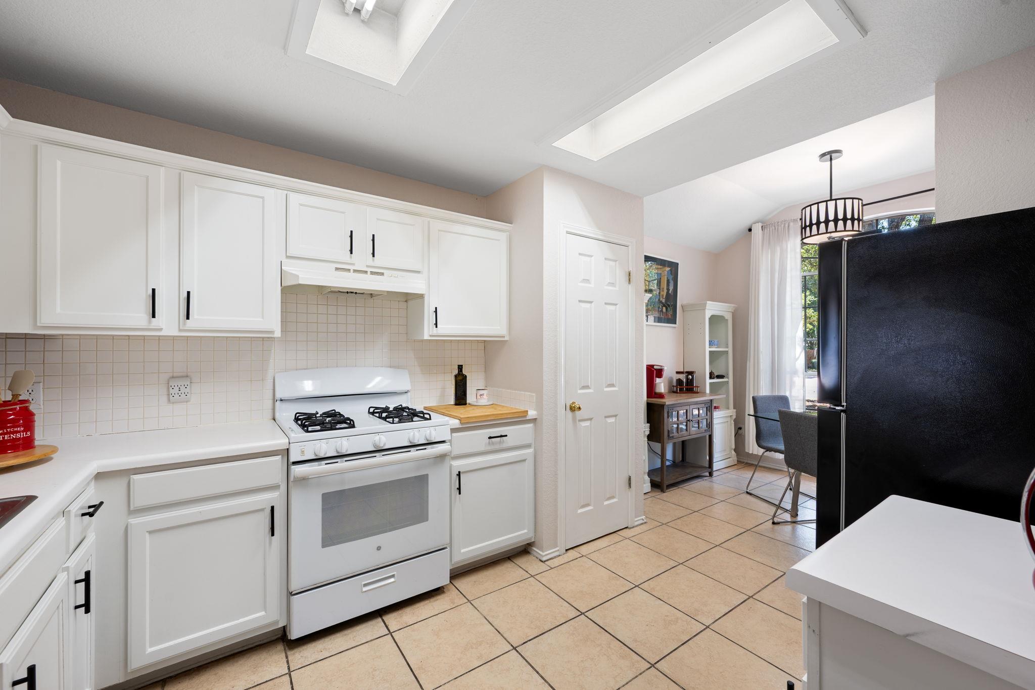 Kitchen with white cabinets, a gas range, tiled backsplash, and adjoining dining nook.