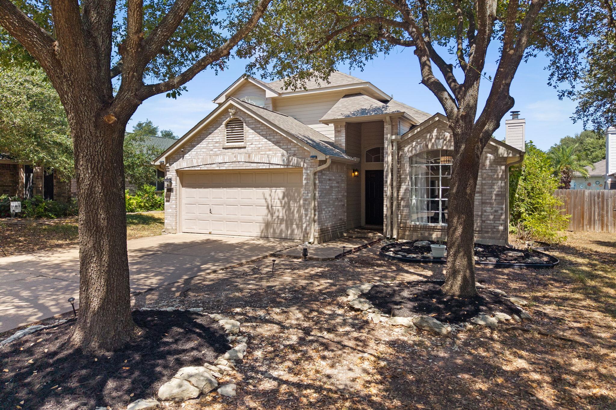 Two-story brick house with a two-car garage, framed by mature shade trees.