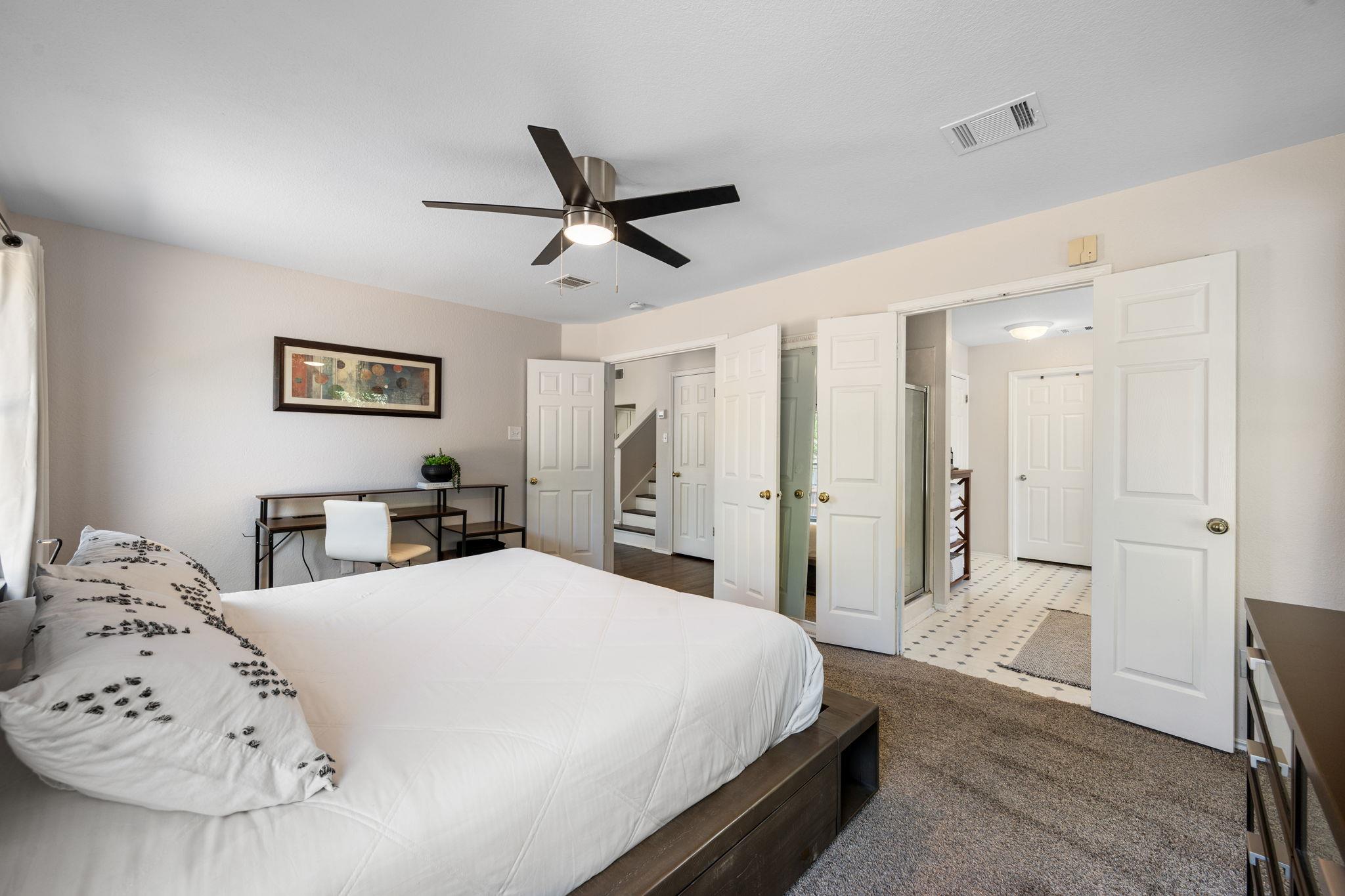 Bedroom with a large white bed and open doors to an adjoining tiled bathroom.