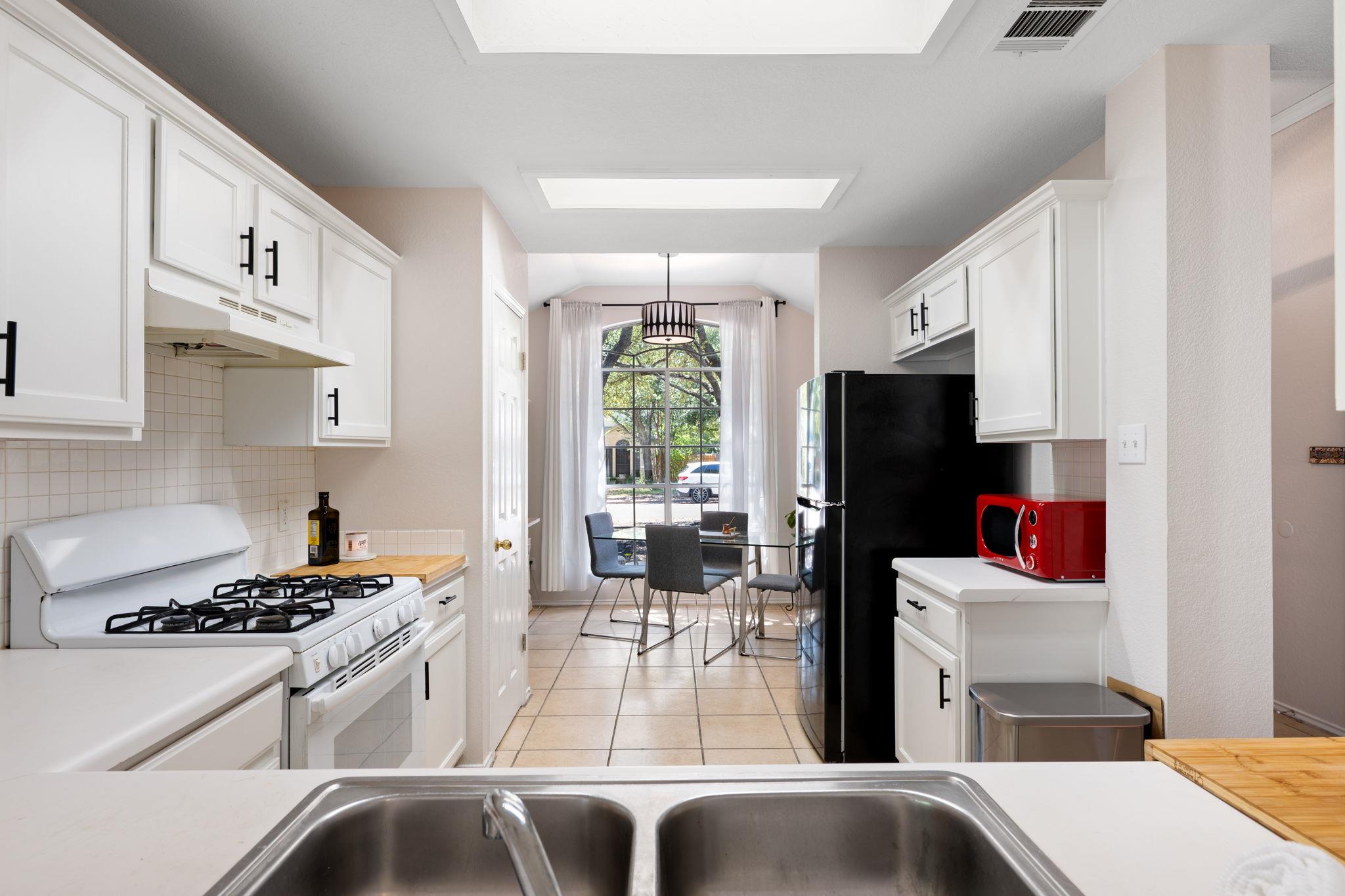 Kitchen with white cabinets, a black refrigerator, and a dining area beside a tall arched window.