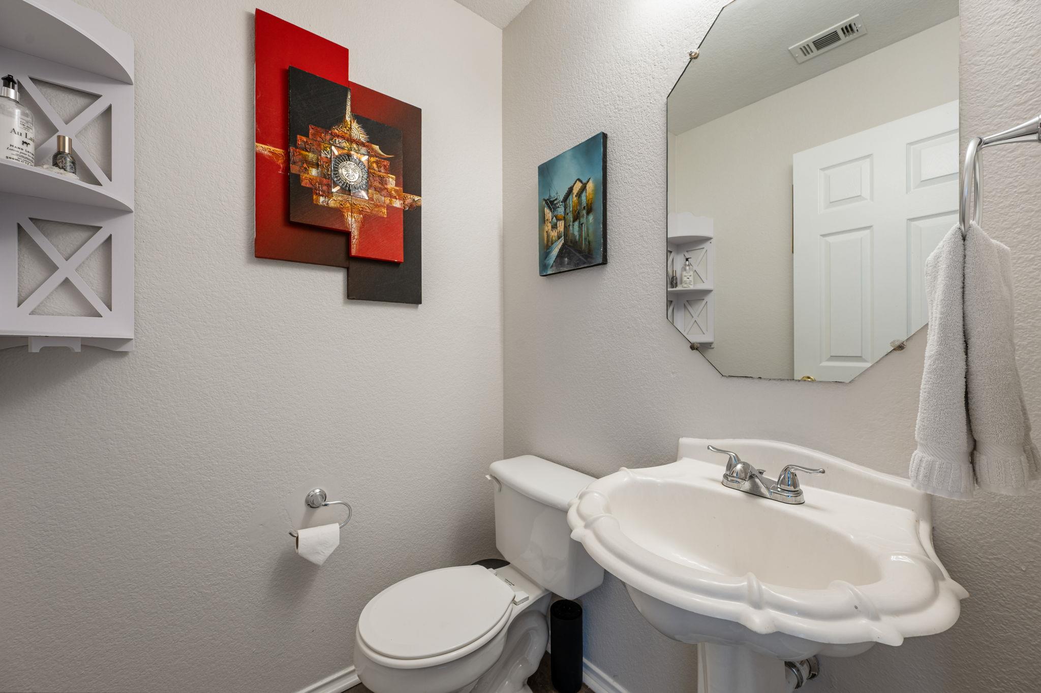 Bathroom with a white pedestal sink, toilet, angular mirror, and colorful wall art.