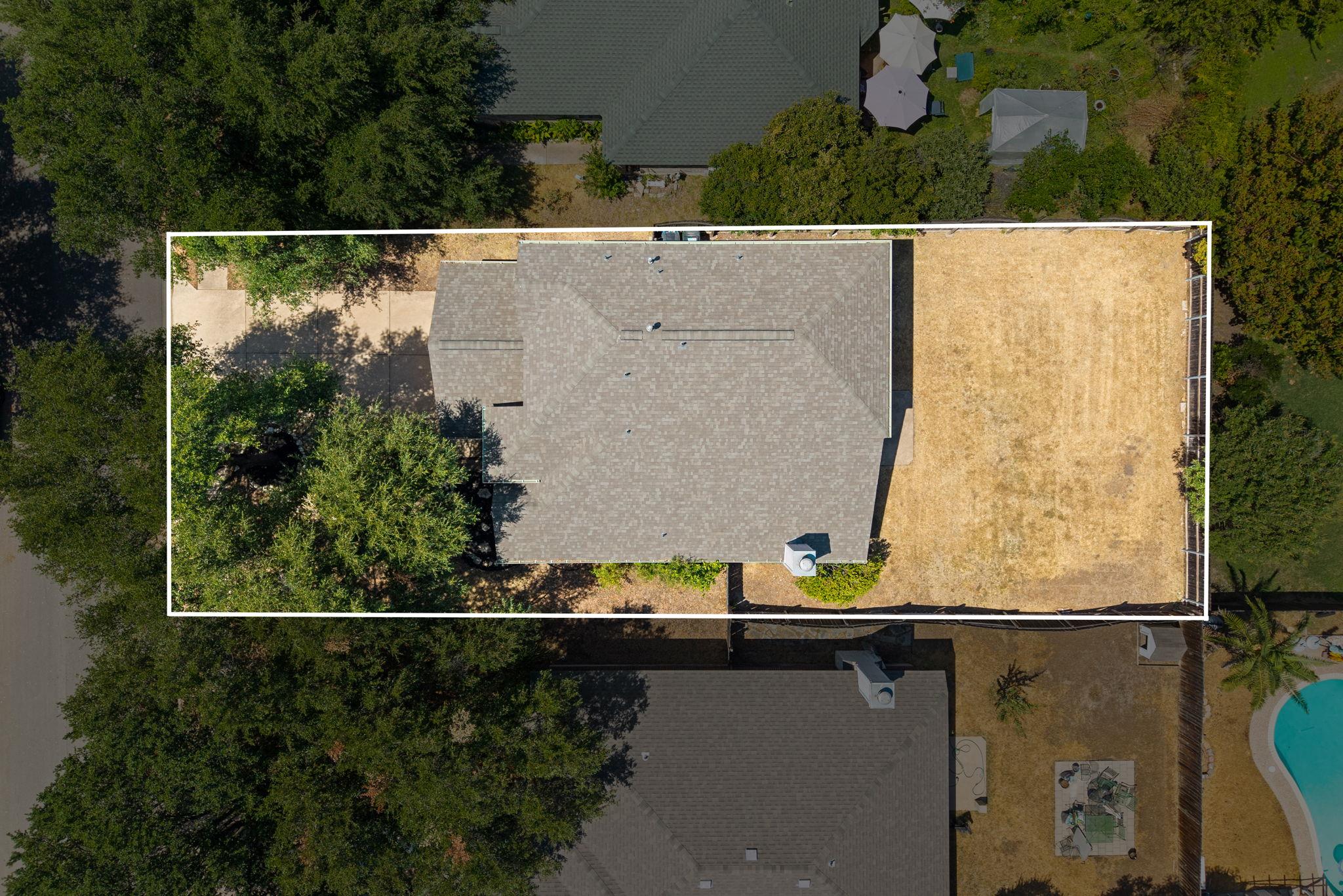Aerial view of a house and lot outlined in white, with a fenced dry lawn and mature trees.