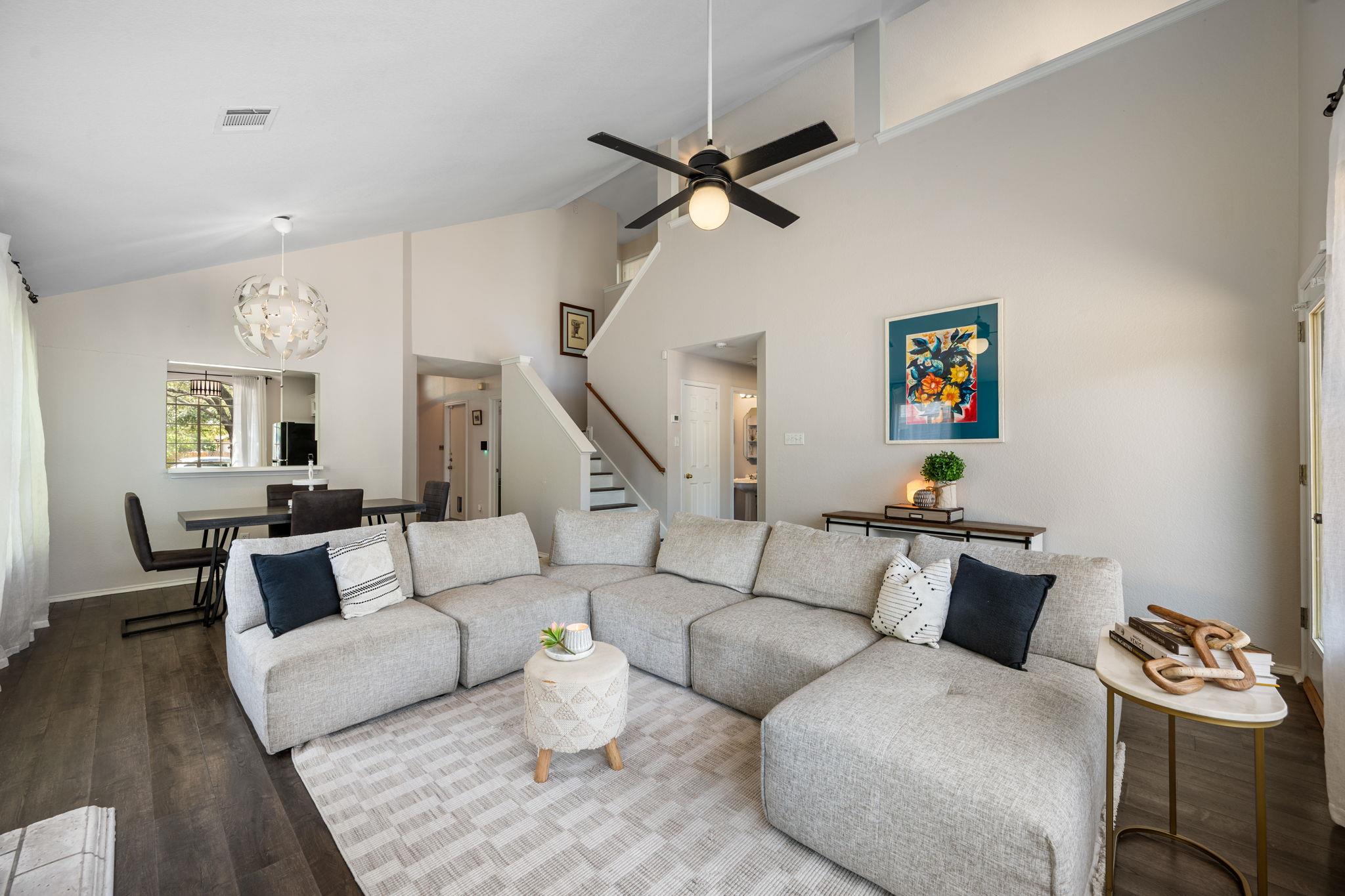 Living room with a large gray sectional beneath a vaulted ceiling, opening to a dining area and staircase.