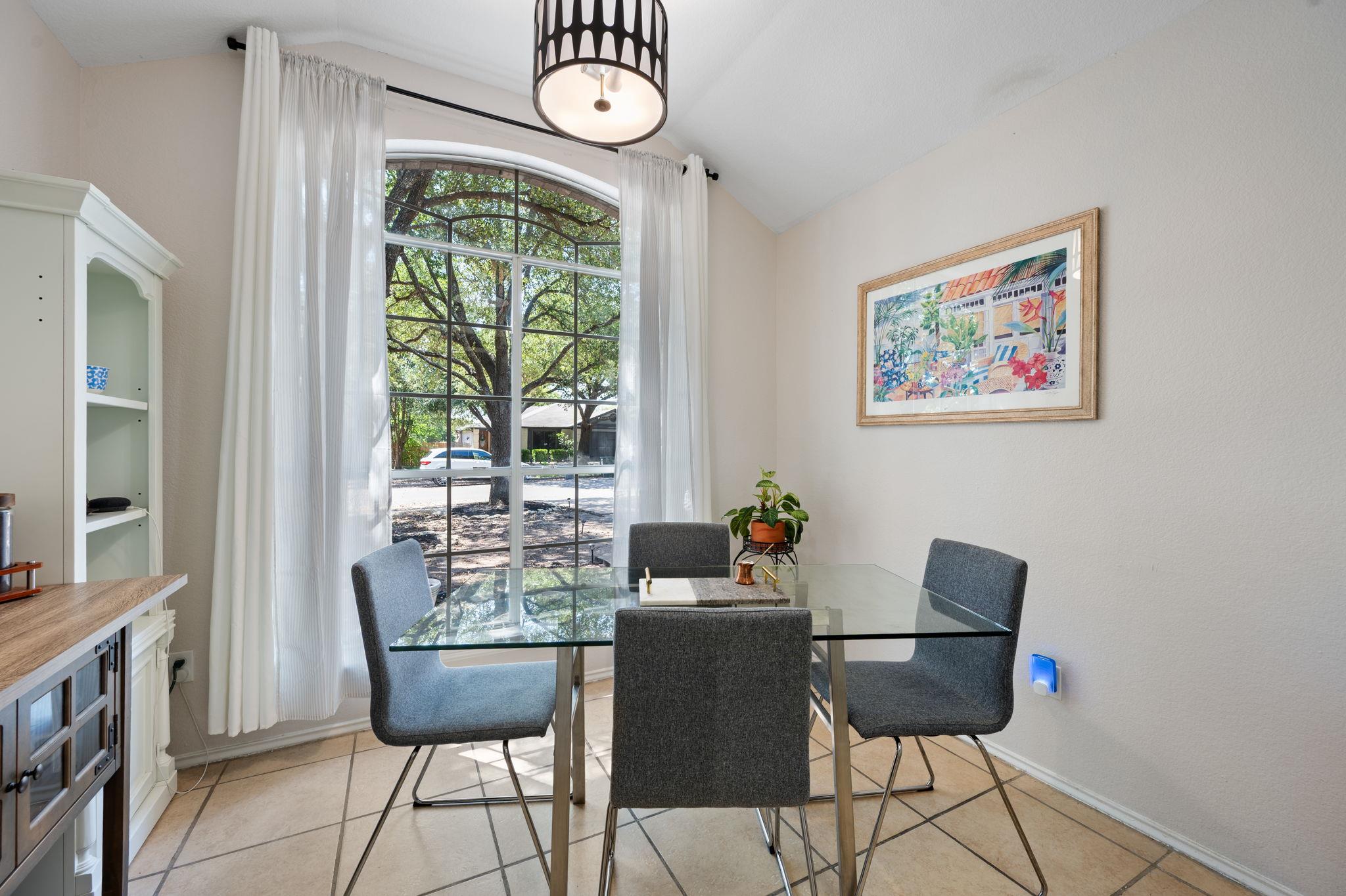 Dining room with a glass-top table, gray chairs, and a tall arched window.