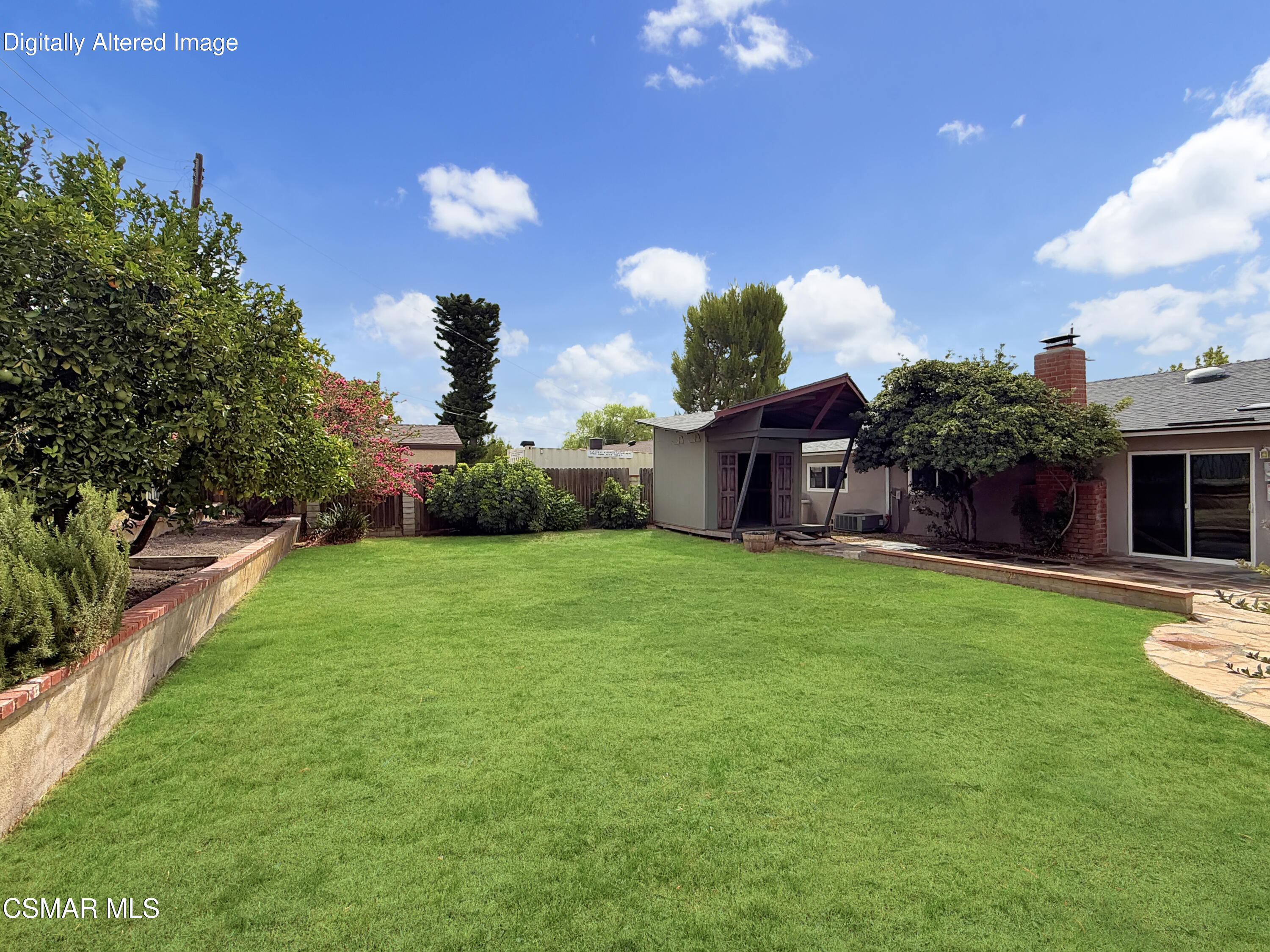 Backyard with a broad green lawn, mature landscaping, and a covered patio structure beside the house.