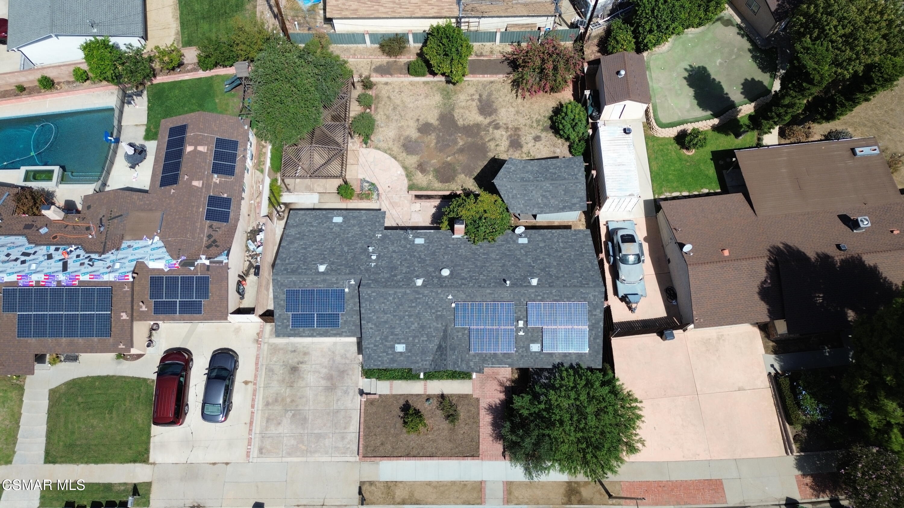 Aerial view of a gray-roofed home with multiple solar panel arrays and a front driveway.