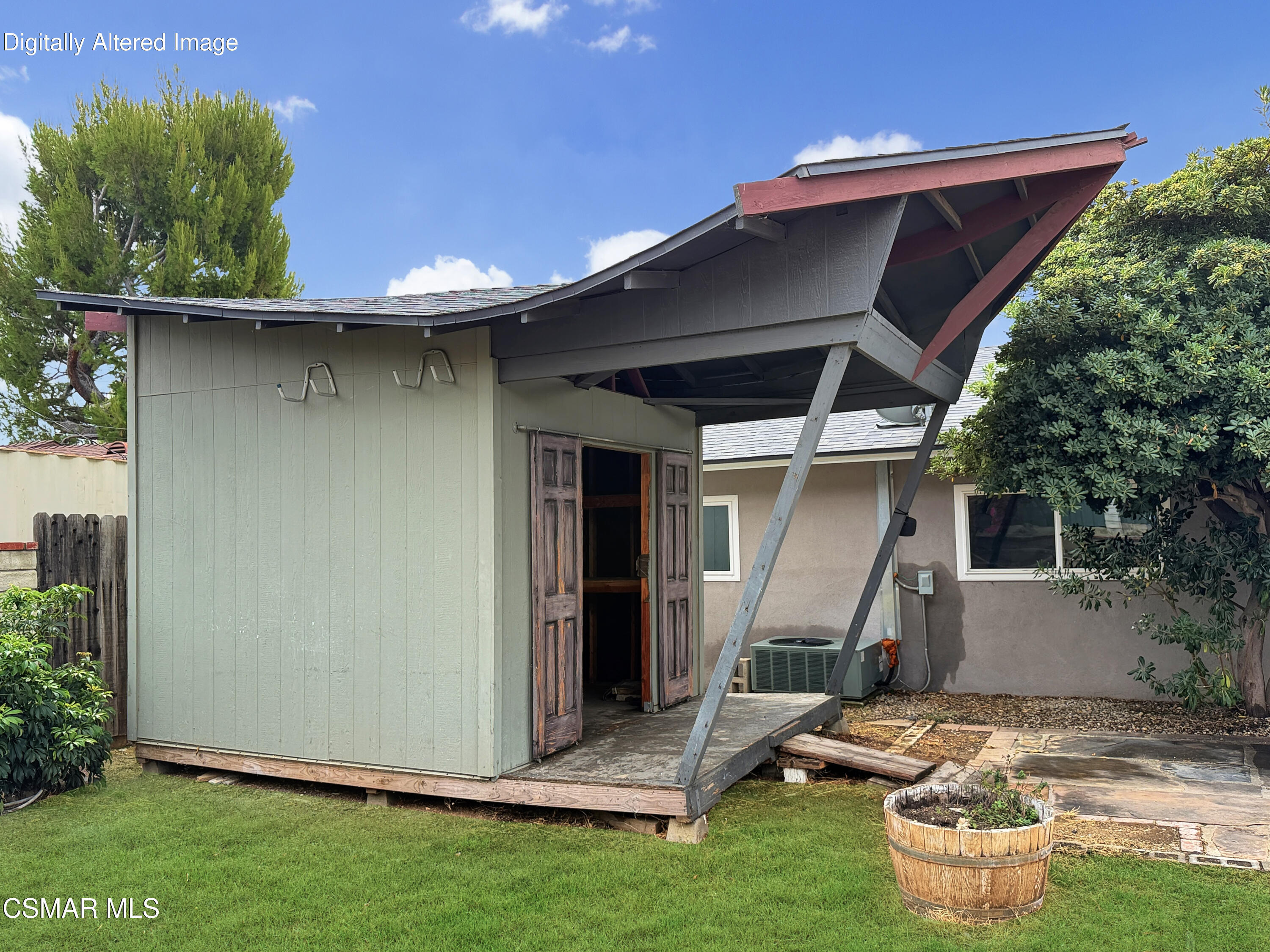 Detached gray backyard shed with weathered doors and a raised red-trimmed roof.