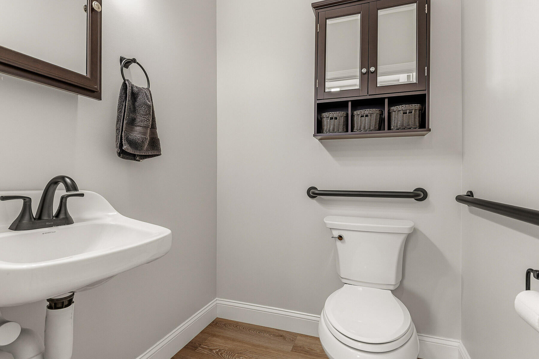 Bathroom with a white sink and toilet, dark grab bars, and a mirrored storage cabinet.