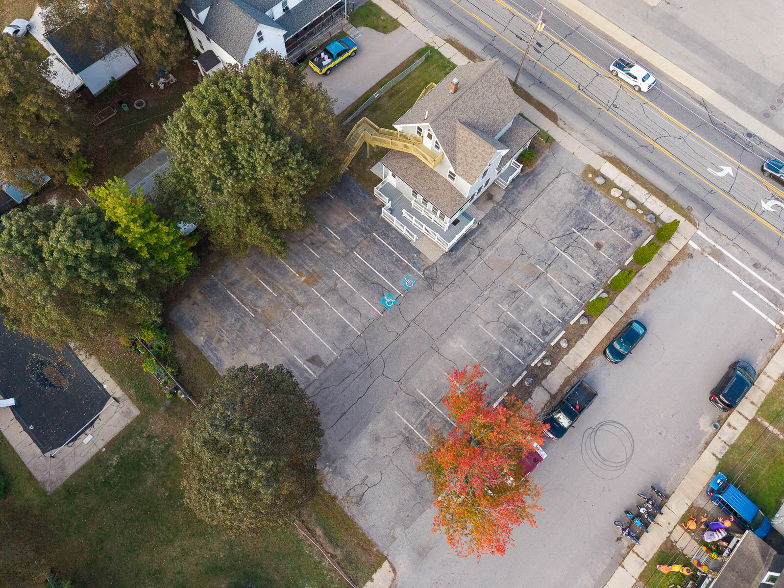 Aerial view of a white multi-story building beside a large parking lot and road.
