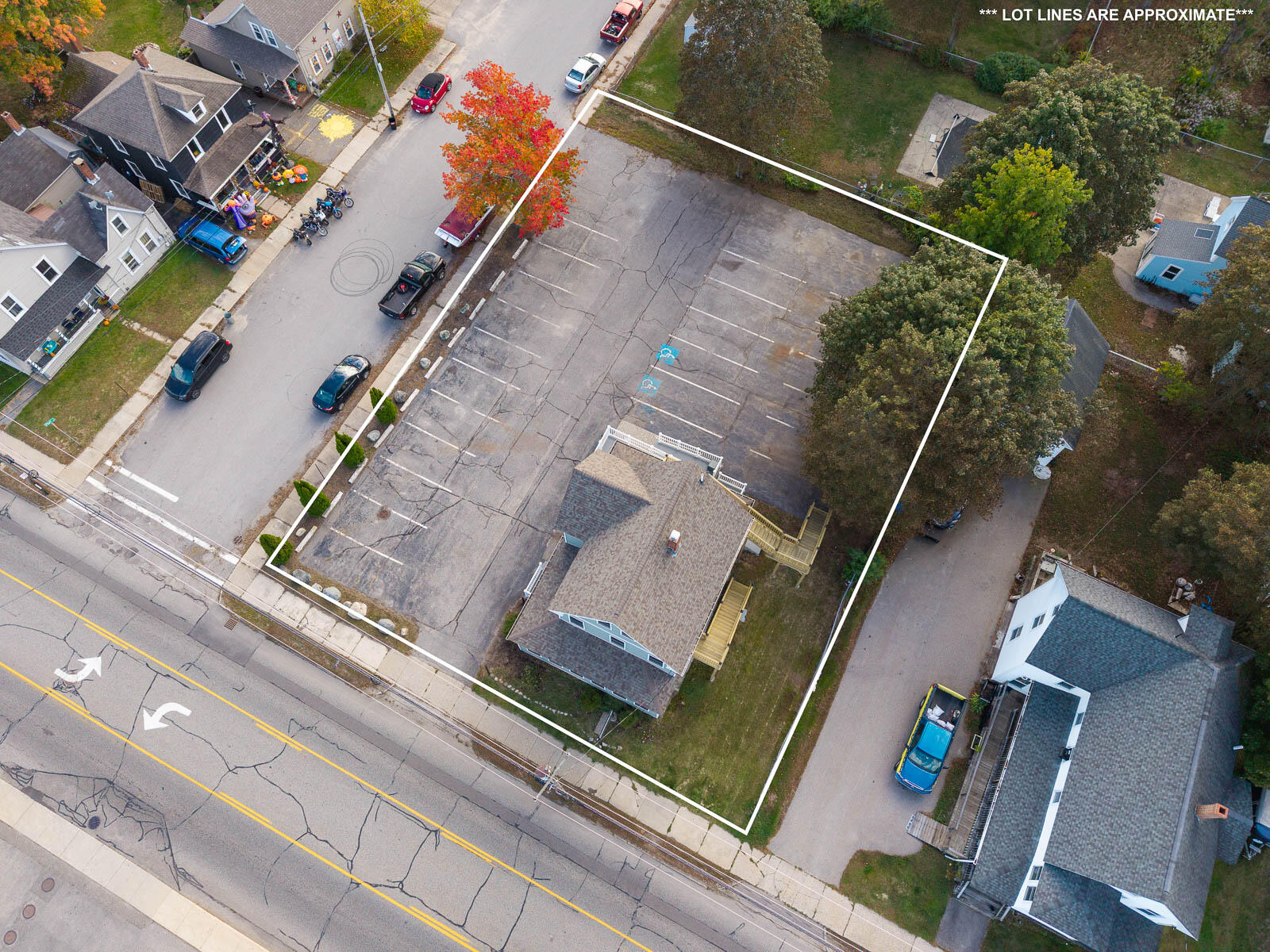 Aerial view of a property outlined with approximate lot lines, showing a large parking lot and a small building.
