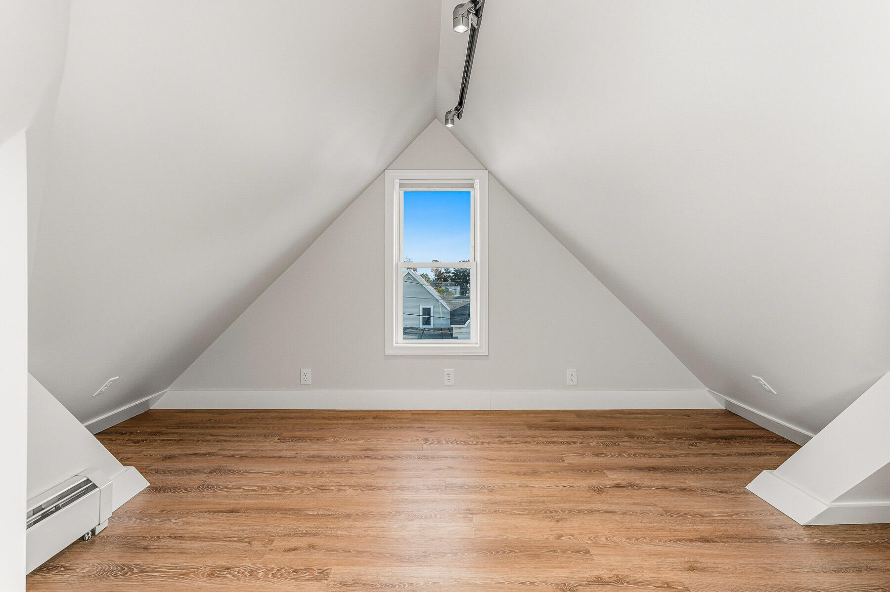 Empty attic room with steep sloped ceilings, wood flooring, and a centered window.