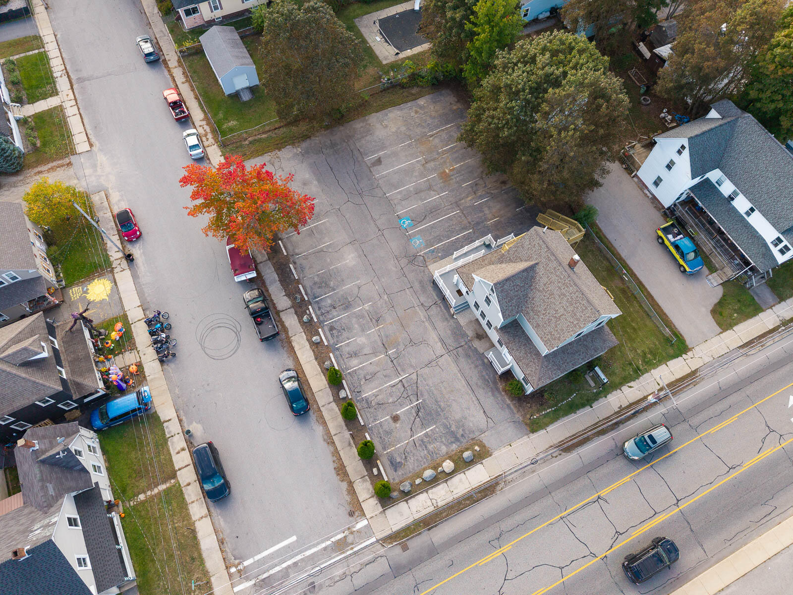 Aerial view of a large paved parking lot beside white buildings and a residential street.