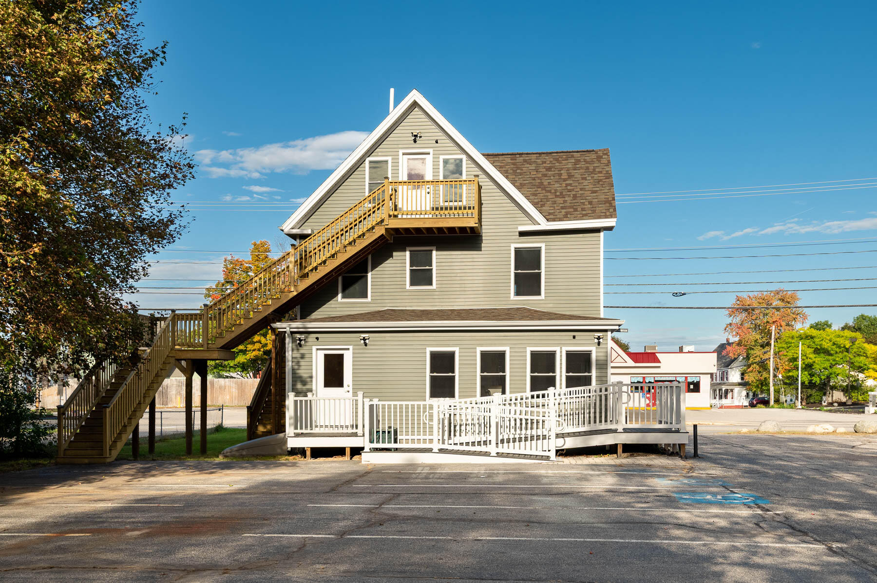 Gray two-story building with a large exterior staircase, upper balcony, and white-railed ramp and deck.