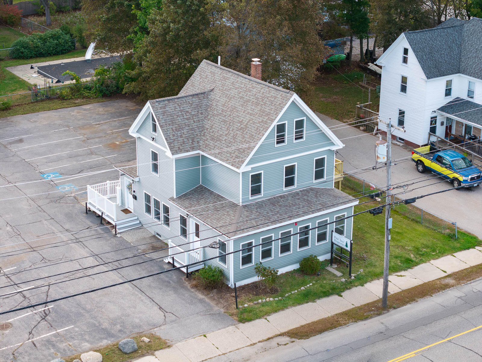 Blue-gray real estate office with a steep shingled roof, parking lot, and roadside sign.