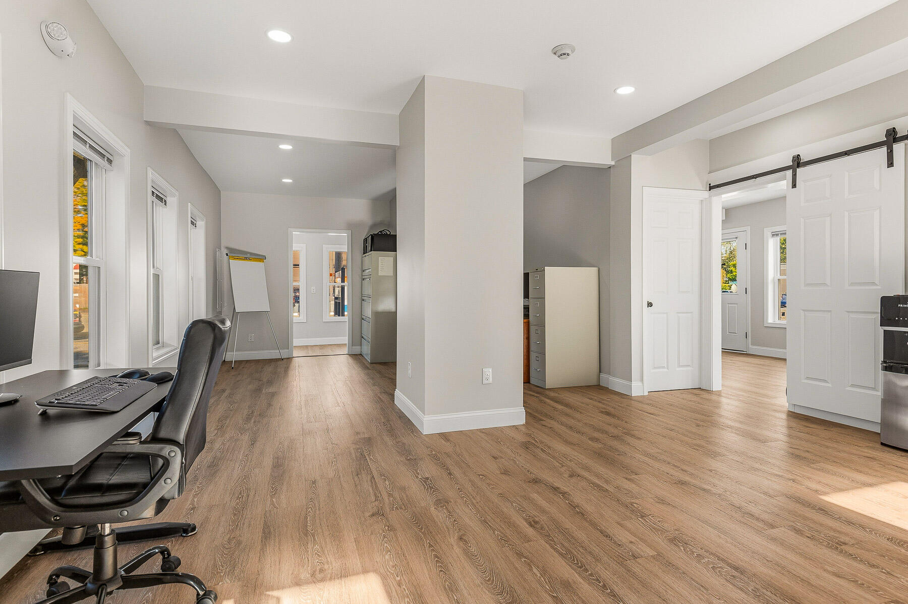 Office interior with wood-look flooring, tall windows, a desk, and a sliding barn door.
