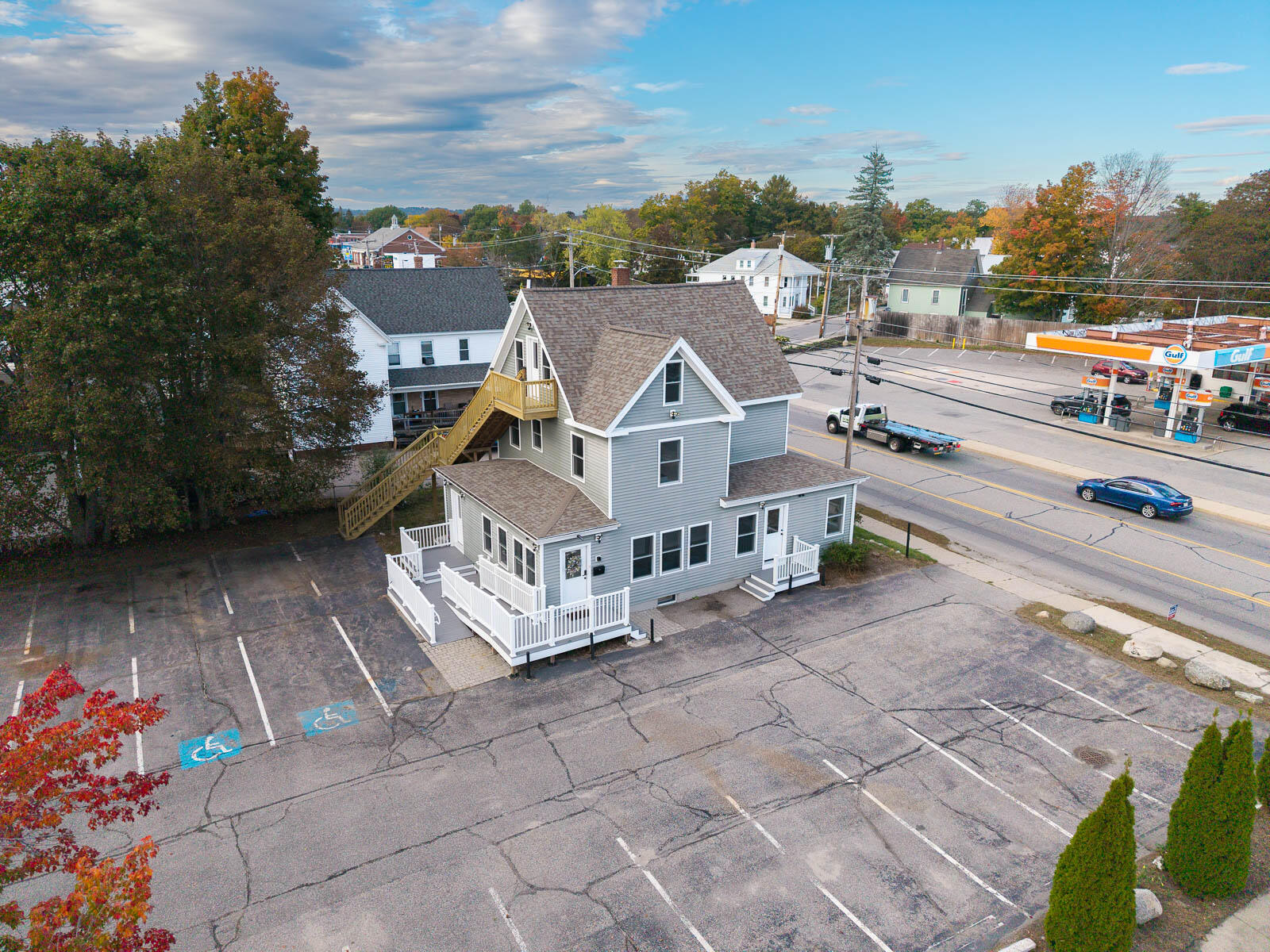 Aerial view of a gray multi-story house with white trim and exterior stairs beside a large parking lot.