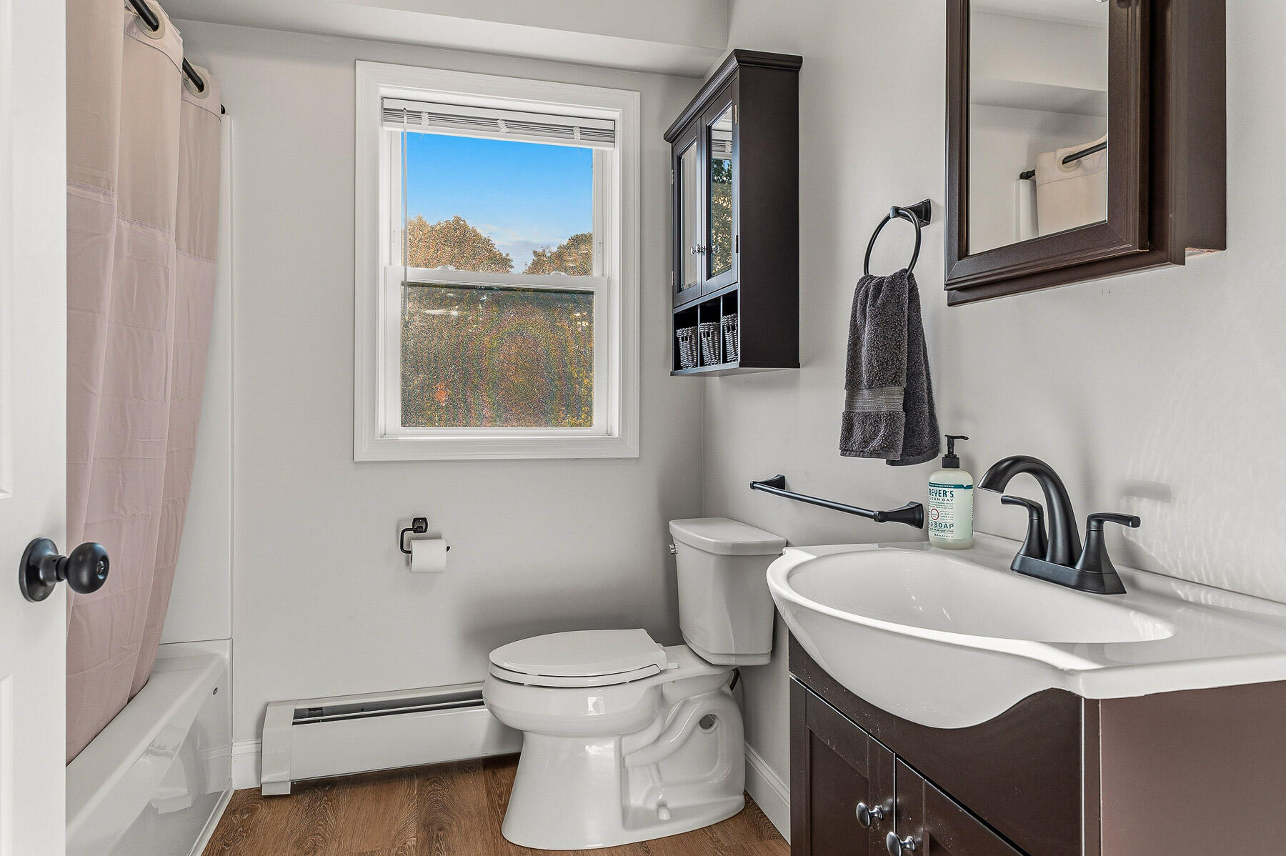 Bathroom with a dark wood vanity, white sink and tub, and a window overlooking autumn trees.