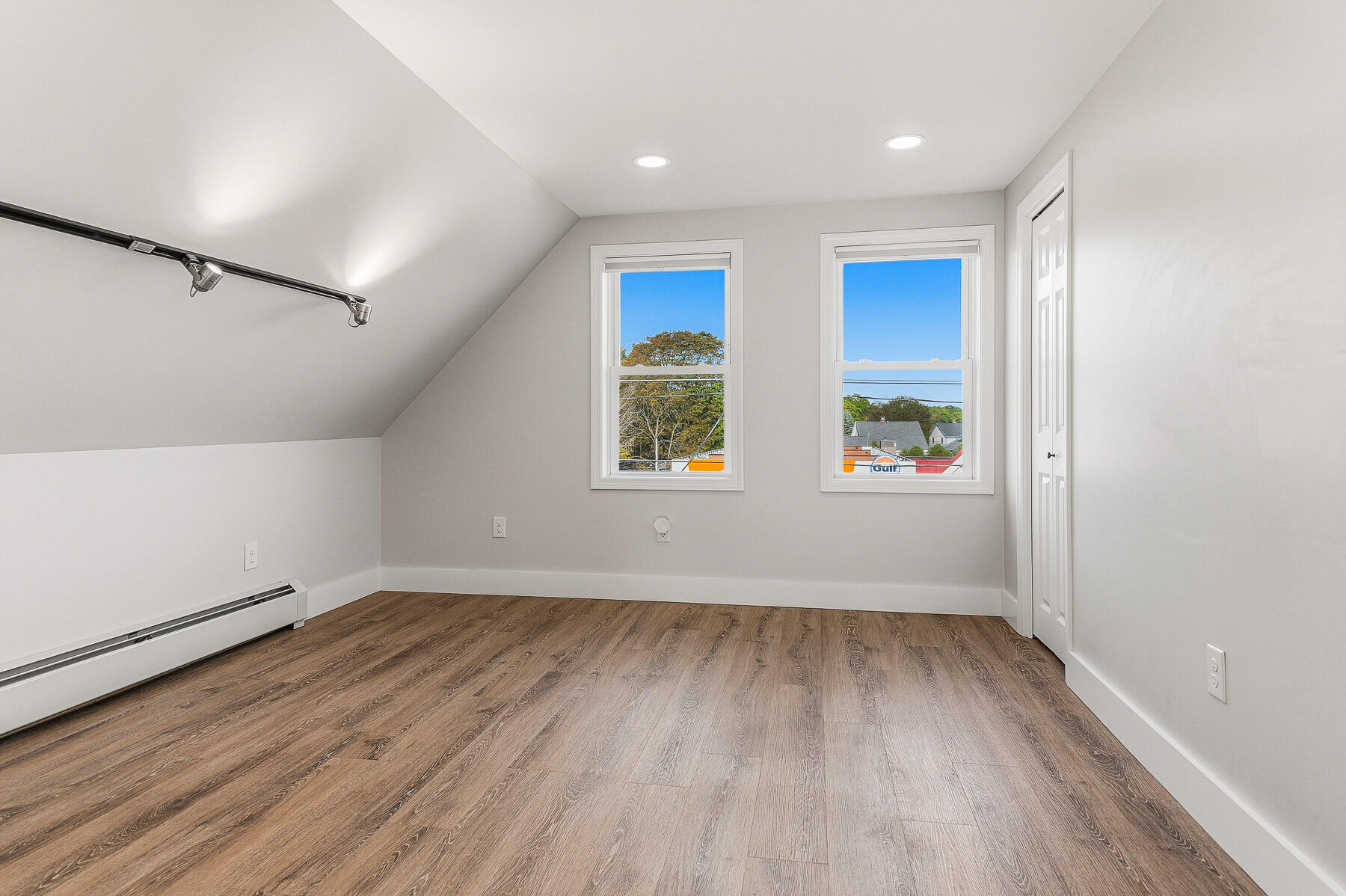 Vacant room with a sloped ceiling, wood-look flooring, two windows, and a small closet.