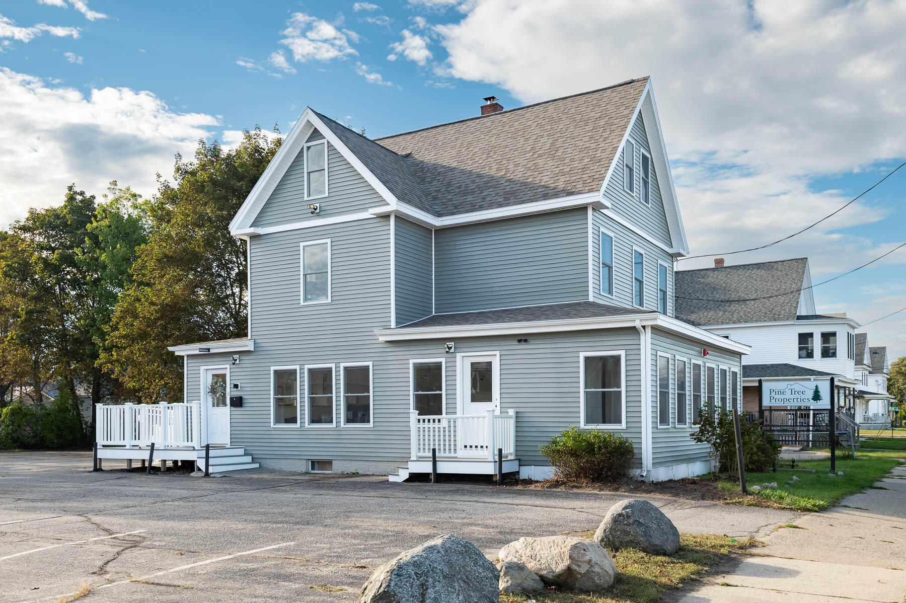 Gray two-story gabled building with white trim, porches, and a Pine Tree Properties sign.