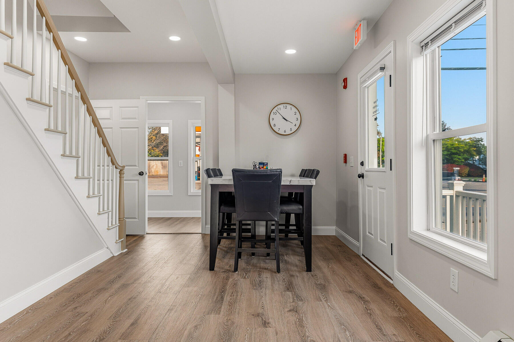Furnished dining area with a staircase, dark table and chairs, and large windows.