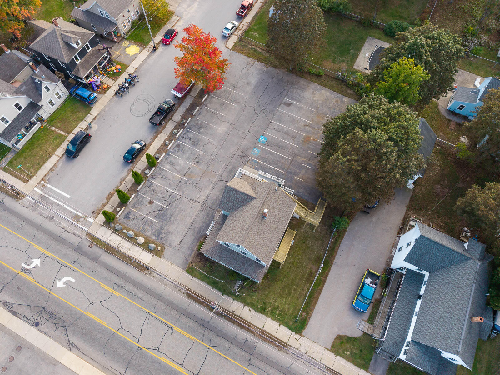 Aerial view of a building and its large parking lot beside a tree-lined street.