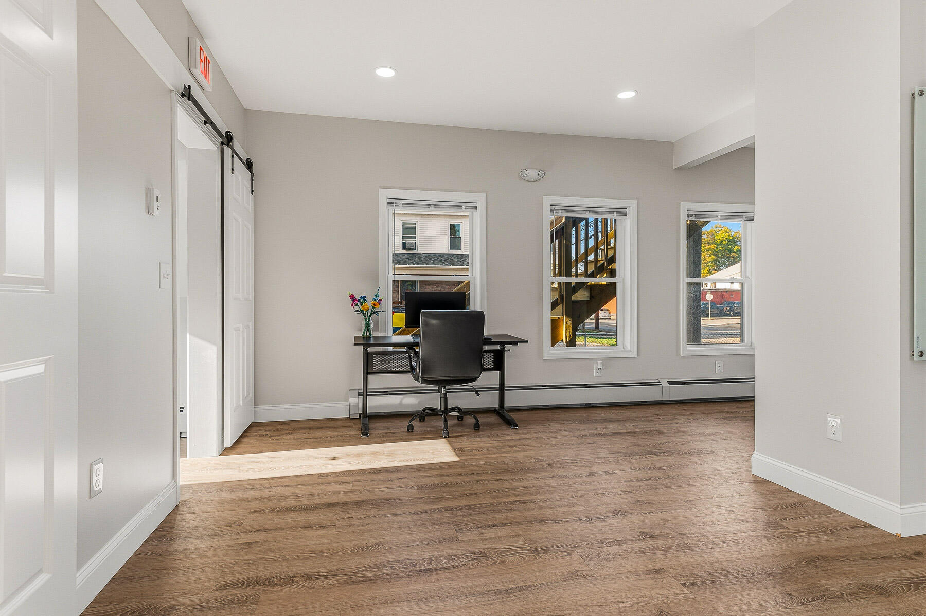Office with a desk and chair, wood-look floors, three windows, and a sliding barn door.